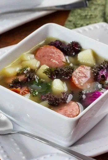 A bowl of vegetable soup with sausage slices and purple cabbage.