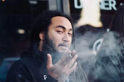 Dread Kennedy smoking a cigarette outdoors with smoke around him.