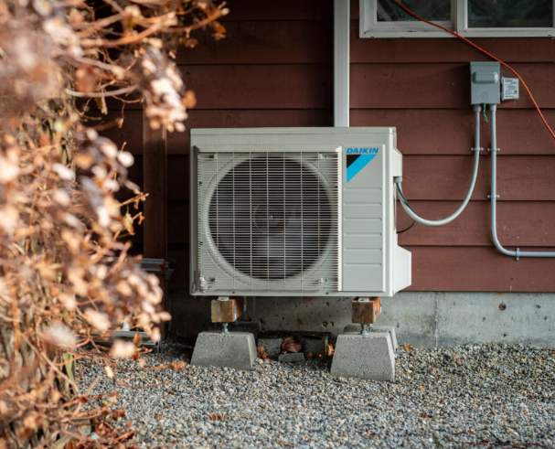 Daikin outdoor air conditioning unit installed on concrete blocks outside a house with red siding.