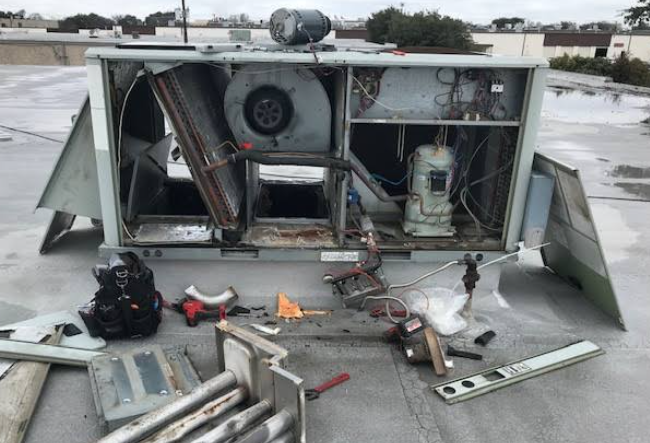 A fallen HVAC unit with exposed internal components, tools, and debris on a flat rooftop surface.