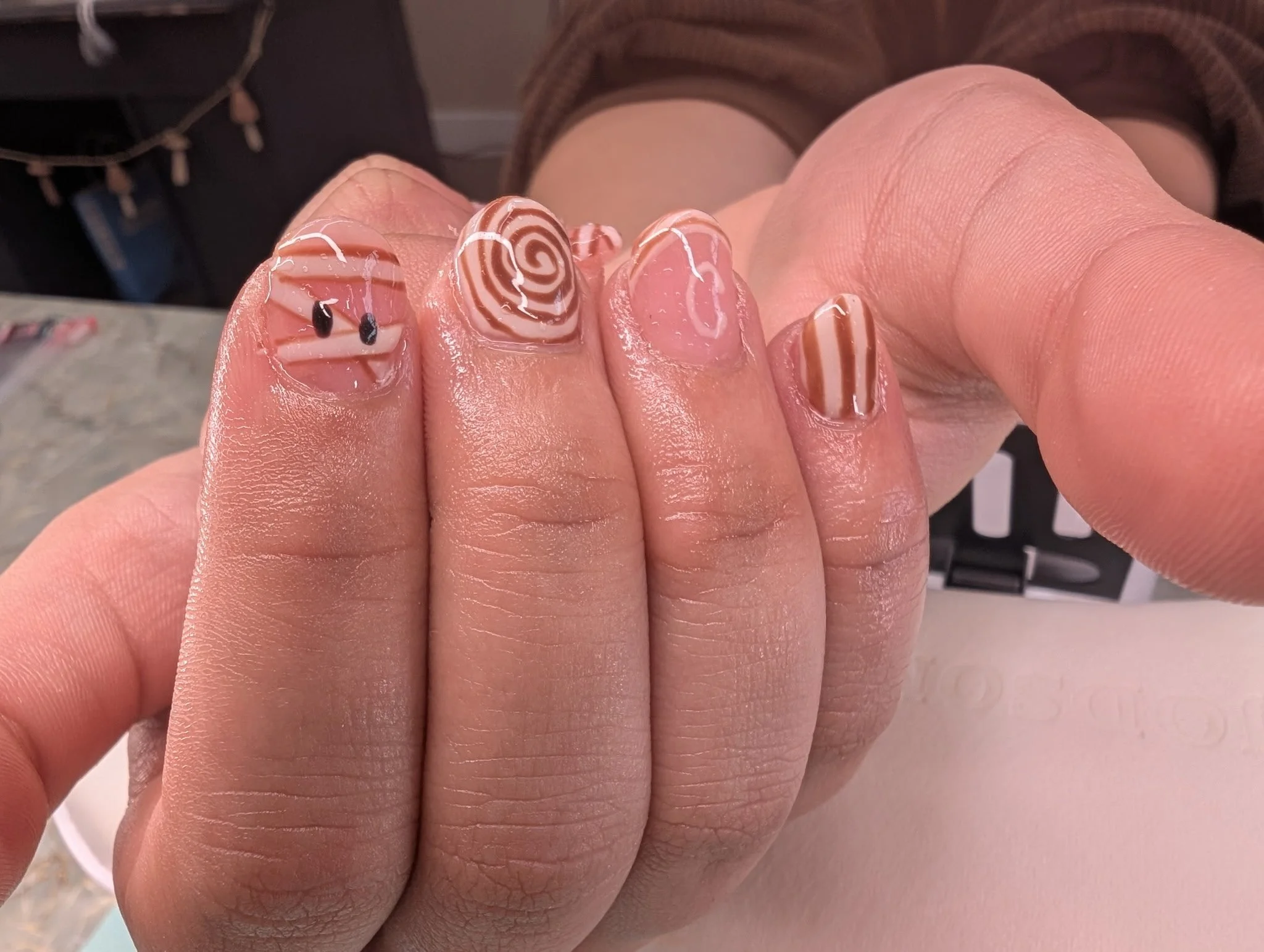 Close-up of a person's hand with decorated nails featuring pink, white, and black designs, including swirls and stripes.