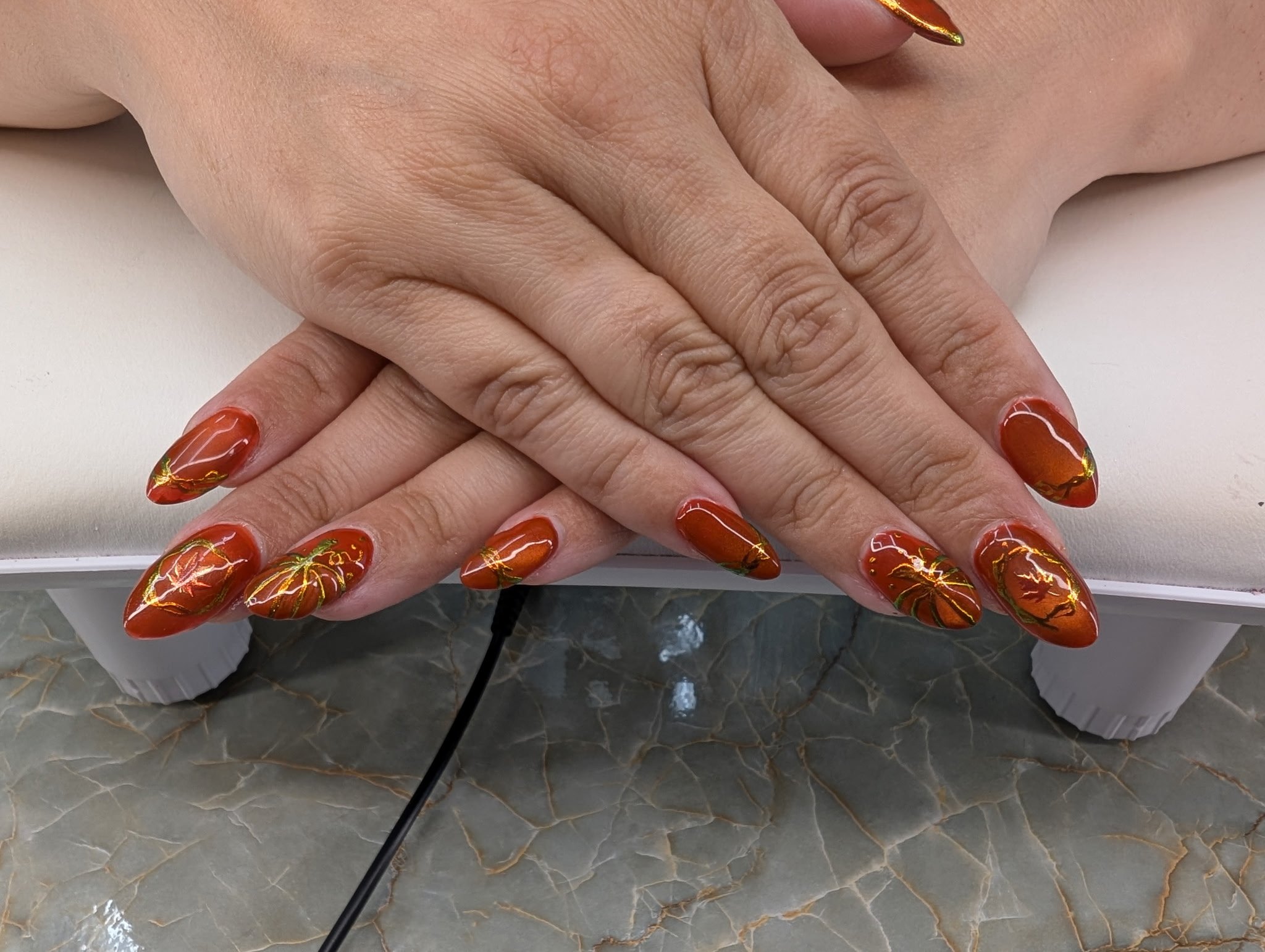 Close-up of a person's hands with red nails featuring a gold branch design, resting on a marble surface.