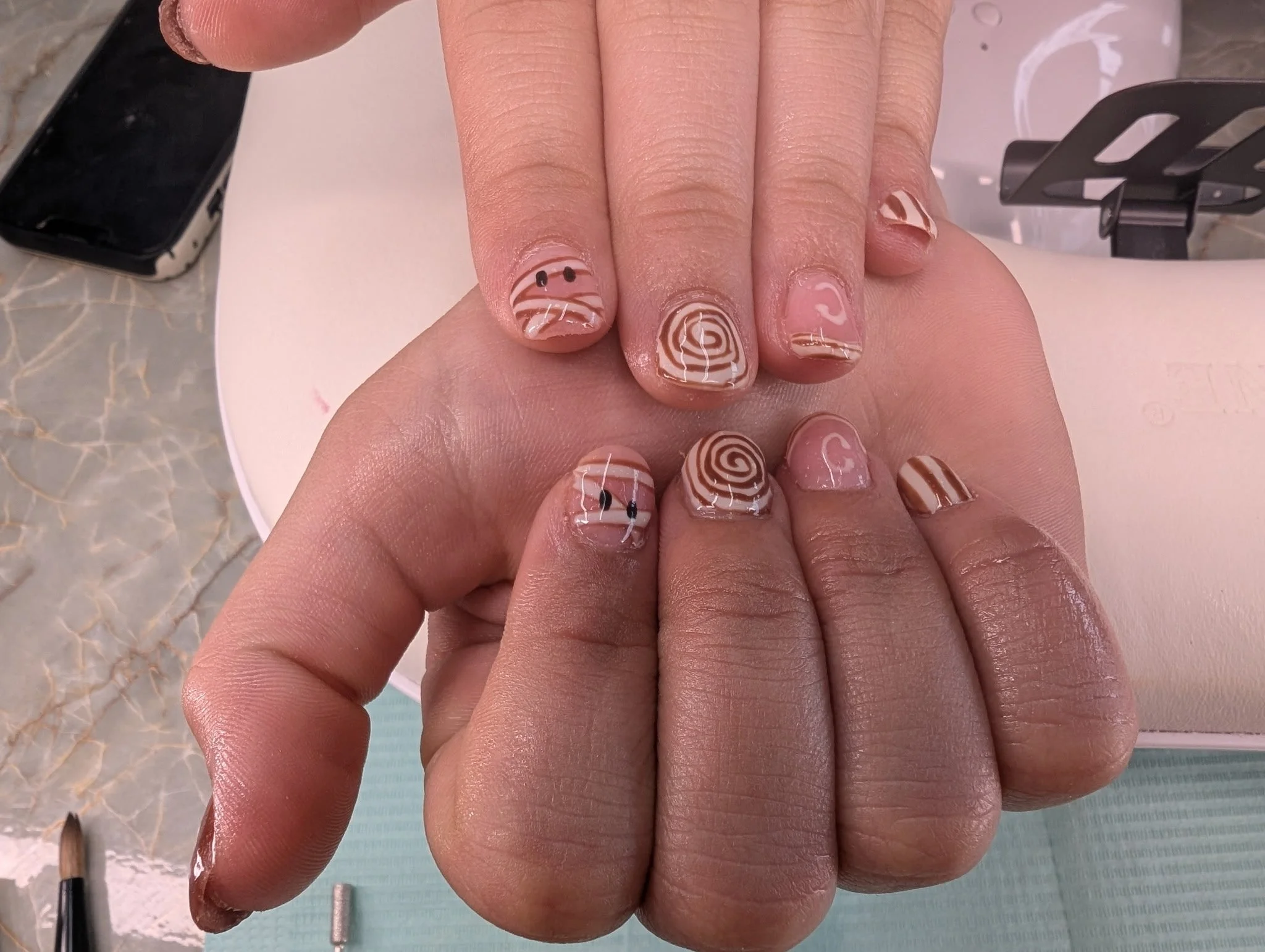 Close-up of a person's hand with decorated nails featuring a marble design with white, beige, and black swirls, and black dots on some nails, over a white surface.