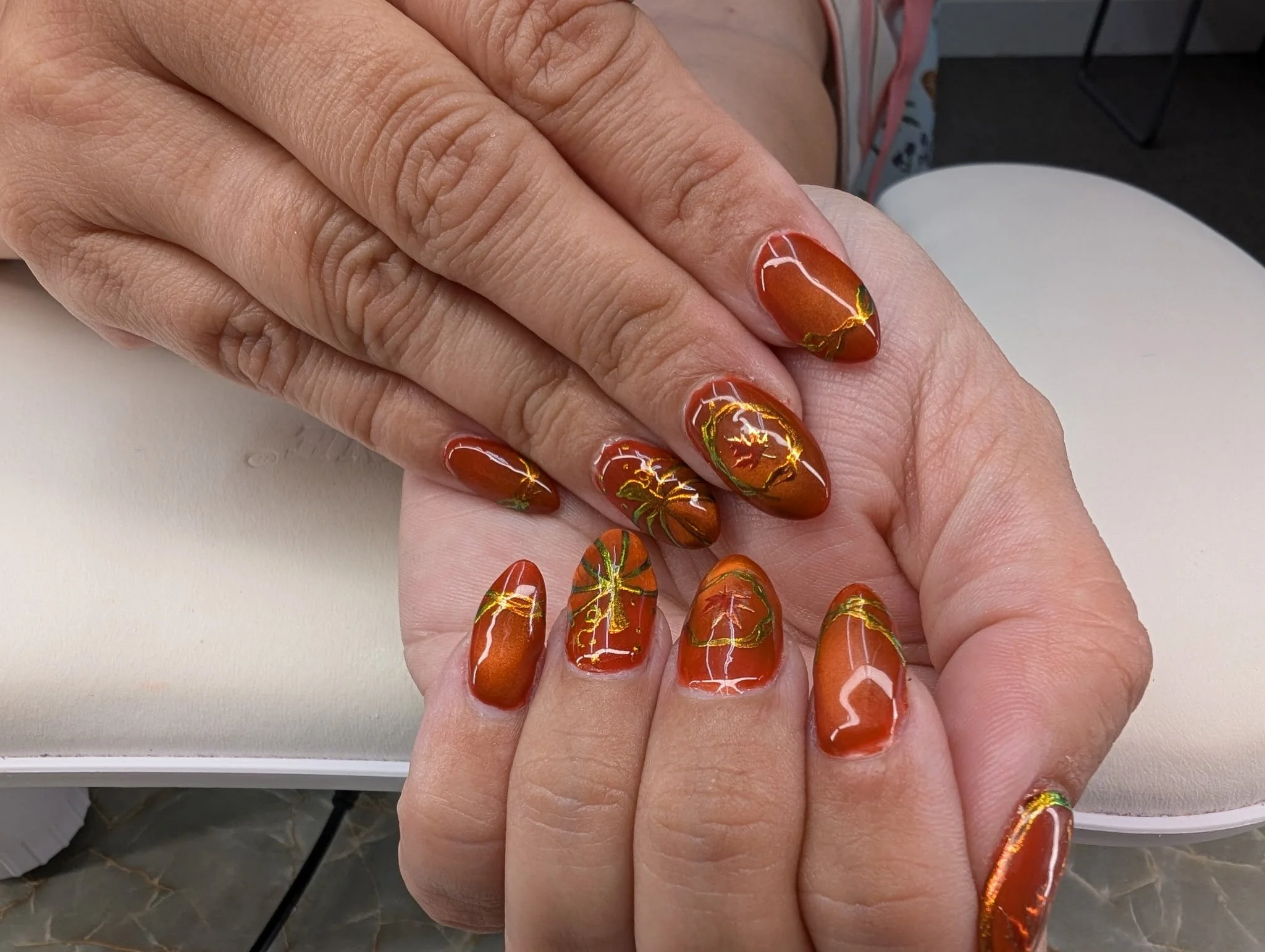 Close-up of a hand with orange and gold leaf nail art on fingernails.