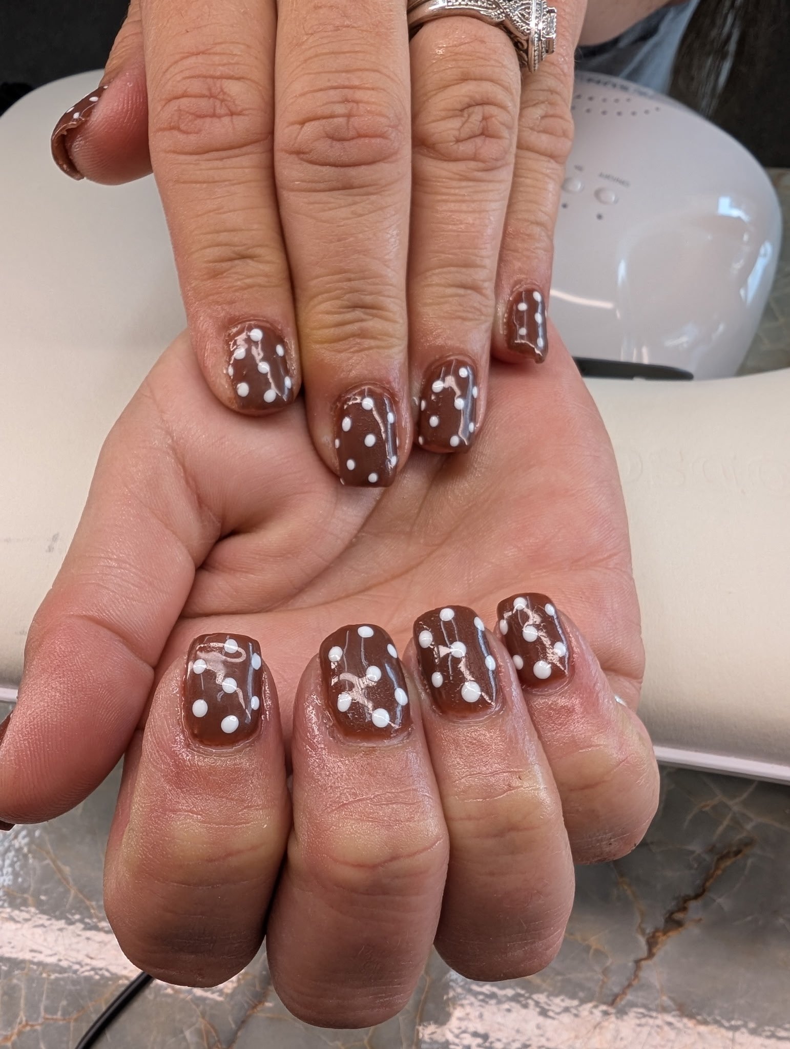 Close-up of a person's hand with nails decorated in brown nail polish with white polka dots.