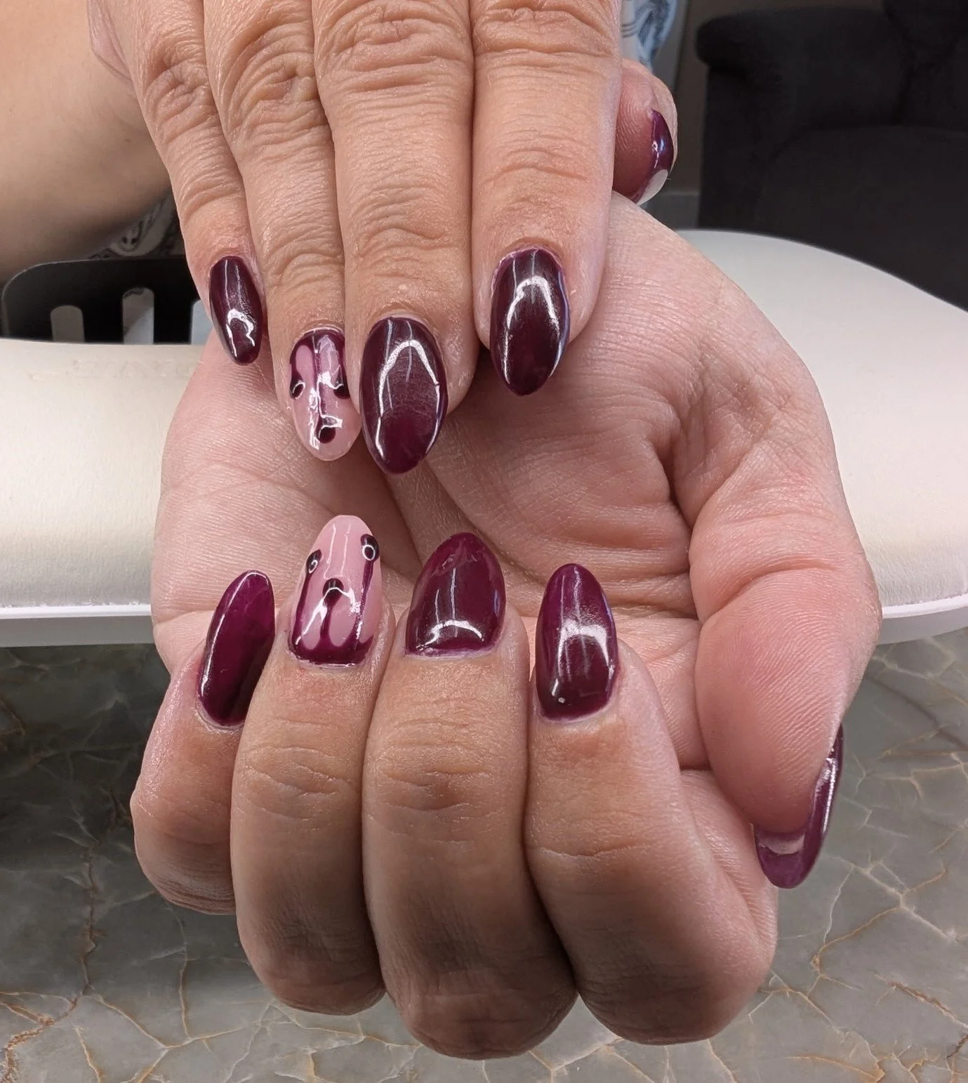 Close-up of hands with manicured nails painted in burgundy and nude with pink and black marble designs.