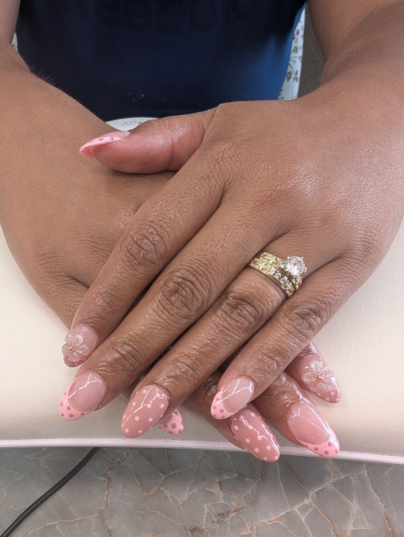 Close-up of two hands with French manicured nails that have pink polish and white swirl and polka dot designs, along with two rings, one with a large clear gemstone ring.