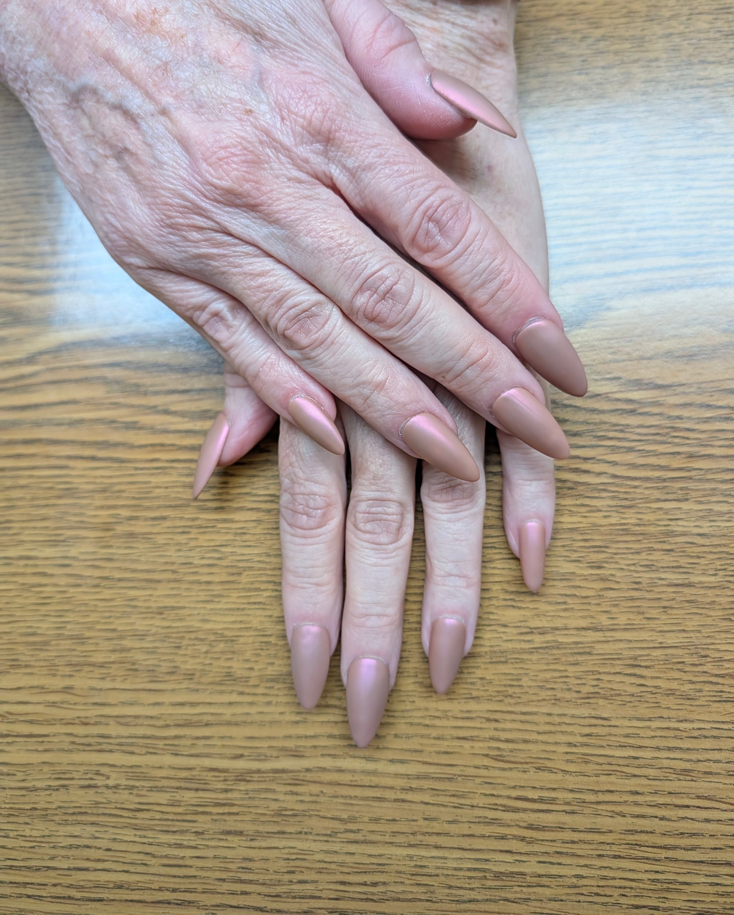 Close-up of a person's hands with long, pointed, pink nails resting on a wooden surface.