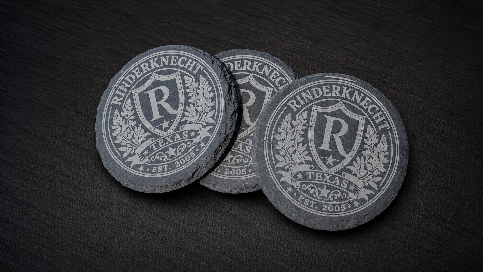 Three round, dark gray, textured coasters or tokens with white engraved design, reading 'RINDERKNECHT,' 'TEXAS,' and 'EST. 2005,' arranged on a dark wooden surface.