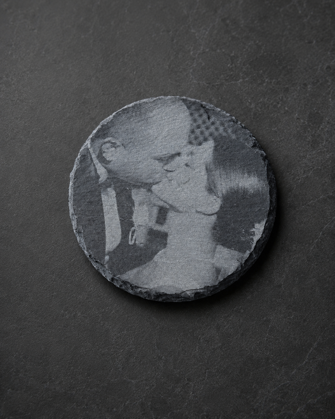 A circular black textured stone with an engraved grayscale image of a young couple kissing.