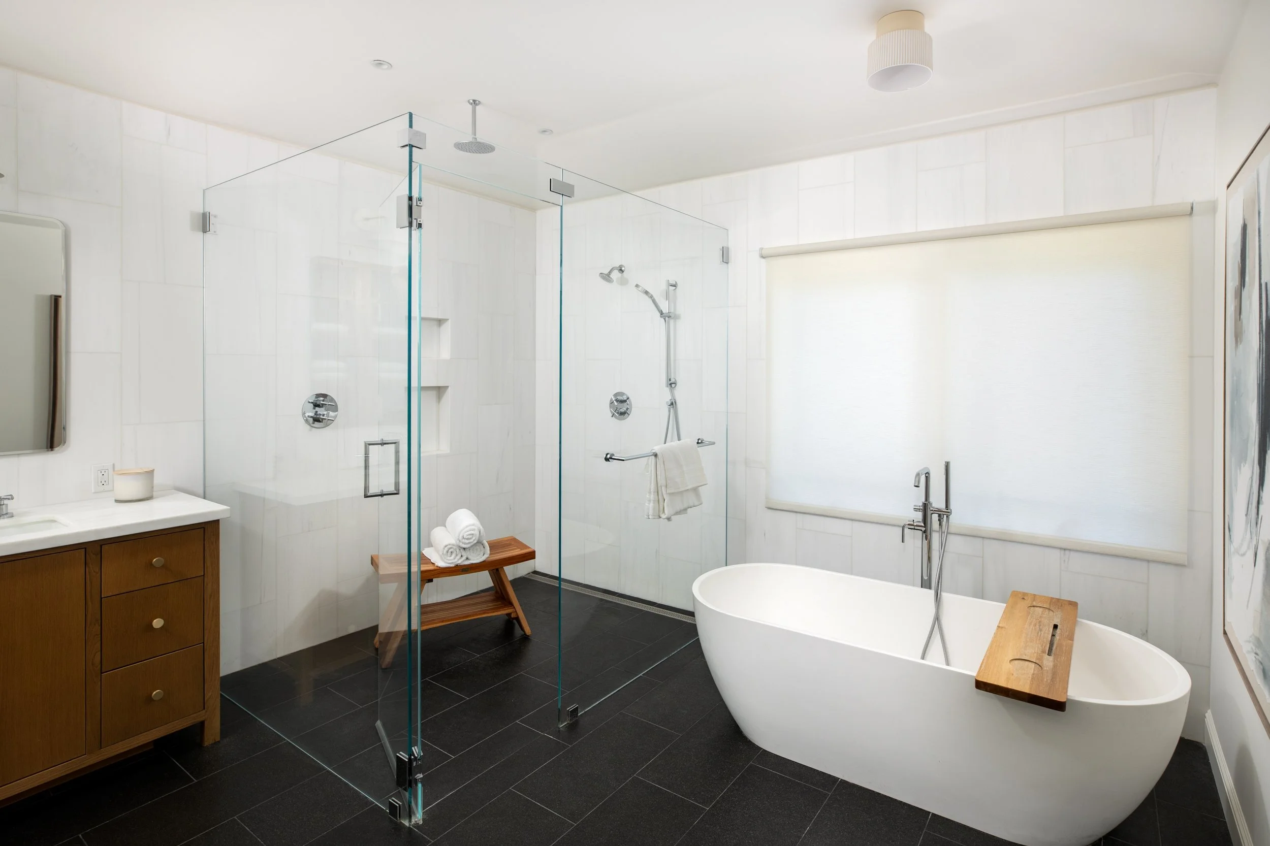 Modern bathroom with a freestanding bathtub, glass shower enclosure, wooden vanity with towels, and black tiled flooring.