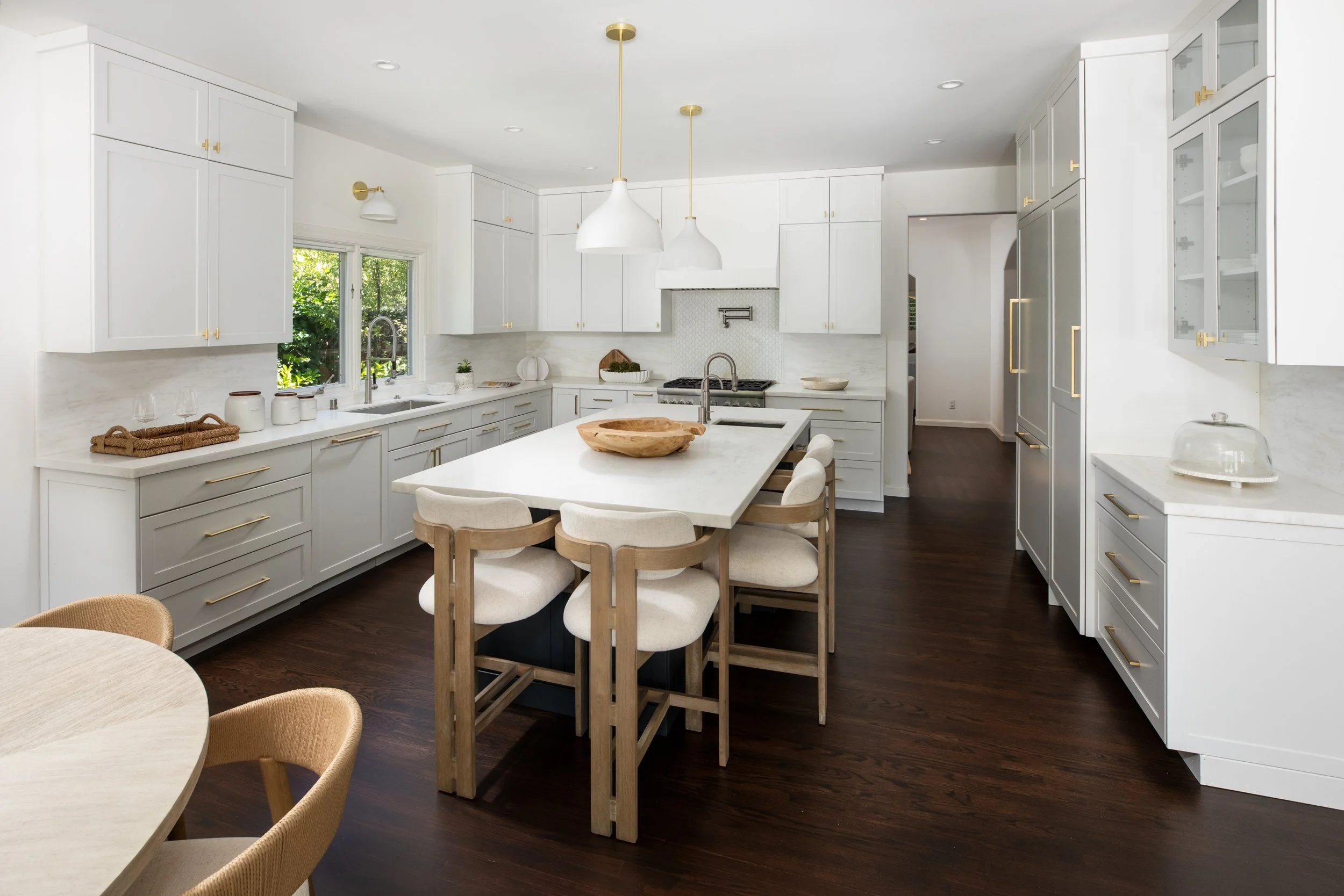 Modern white kitchen with dark hardwood floors, island with a wooden bowl, pendant lights, and built-in cabinets.