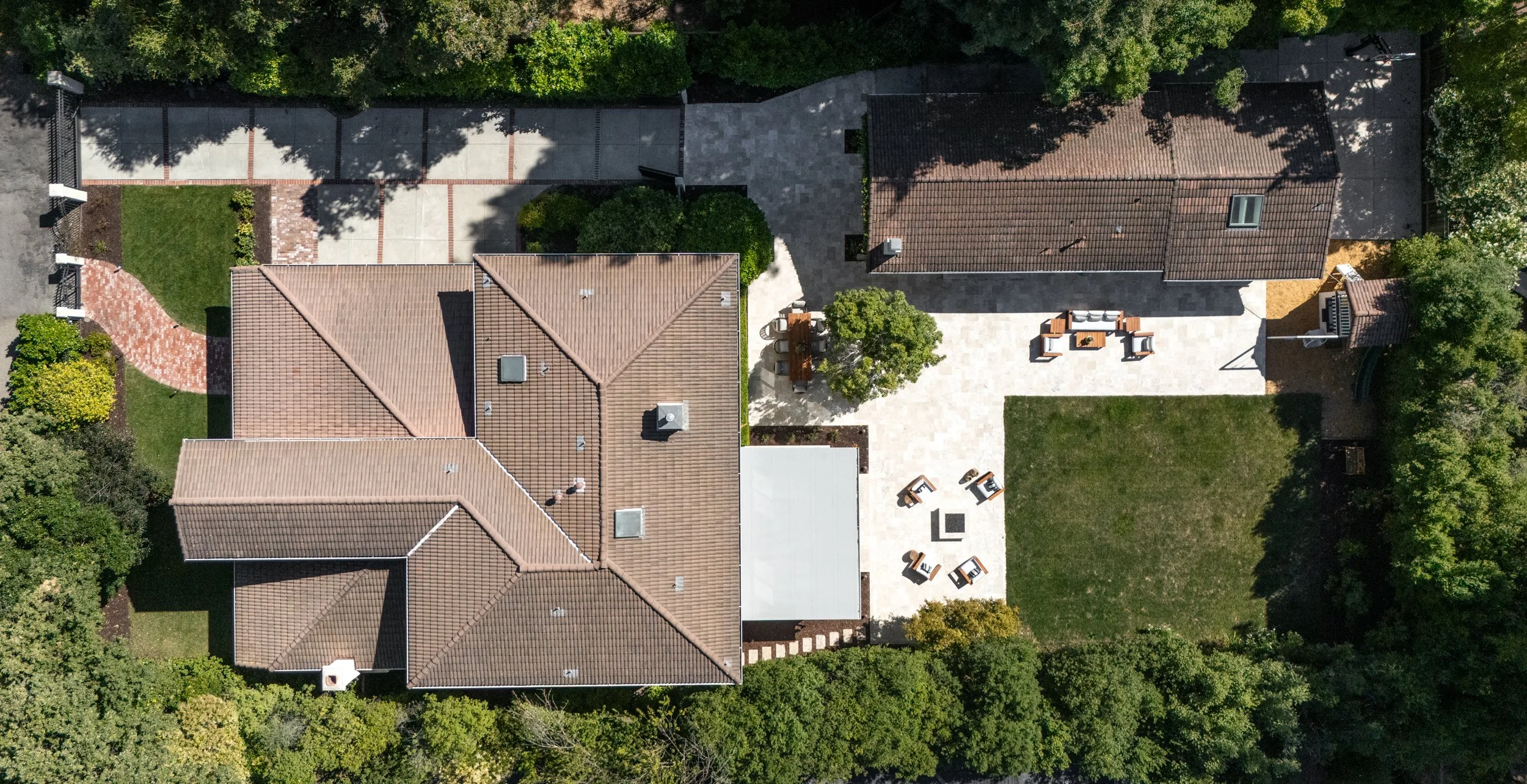 Aerial view of a residential backyard with a patio, seating area, and surrounding greenery.