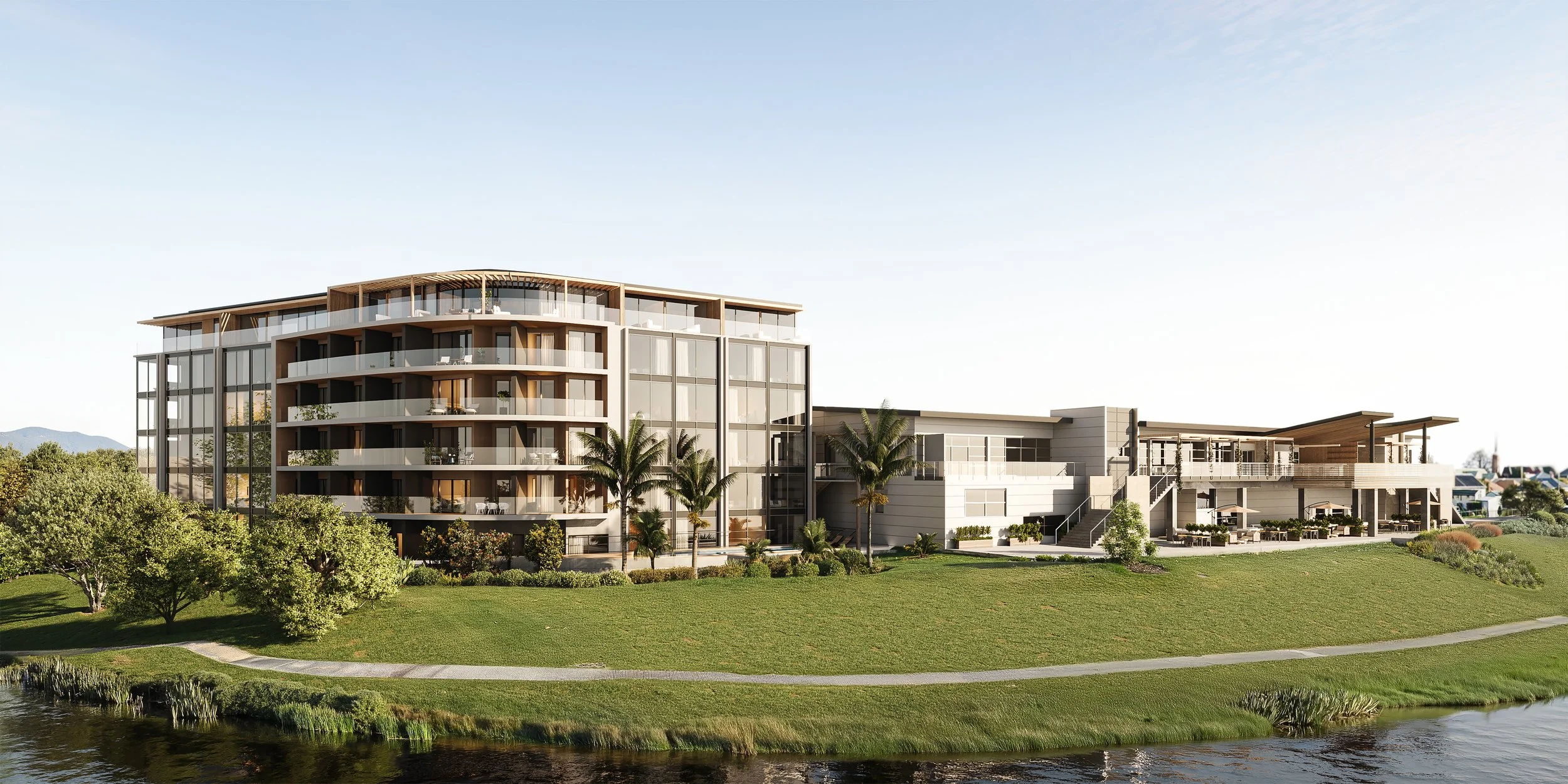 Modern multi-story building with glass windows and balconies, surrounded by green landscape and palm trees, near a small body of water.