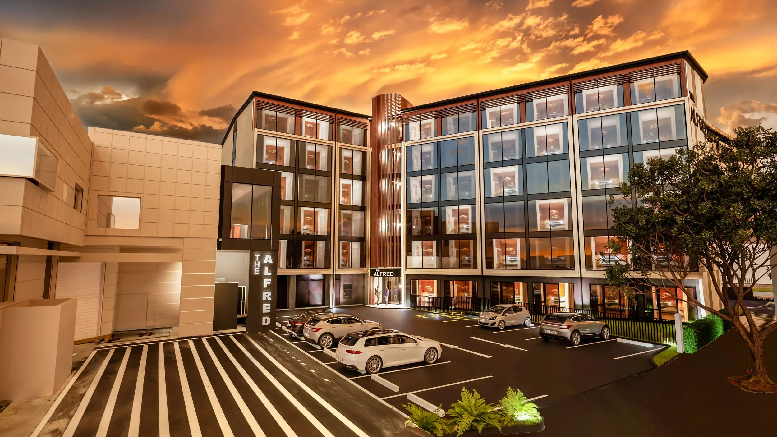 Modern multi-story building at sunset with large glass windows, a parking lot with several cars, and a tree in the foreground.