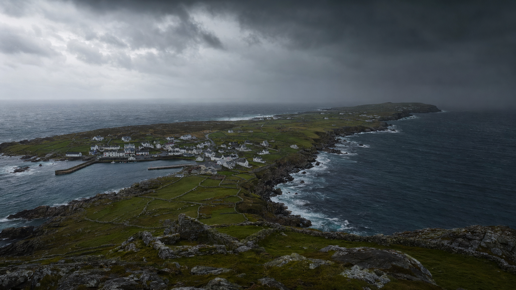 A coastal village with white buildings and green fields under a dark, cloudy sky, bordered by rocky cliffs and the ocean.