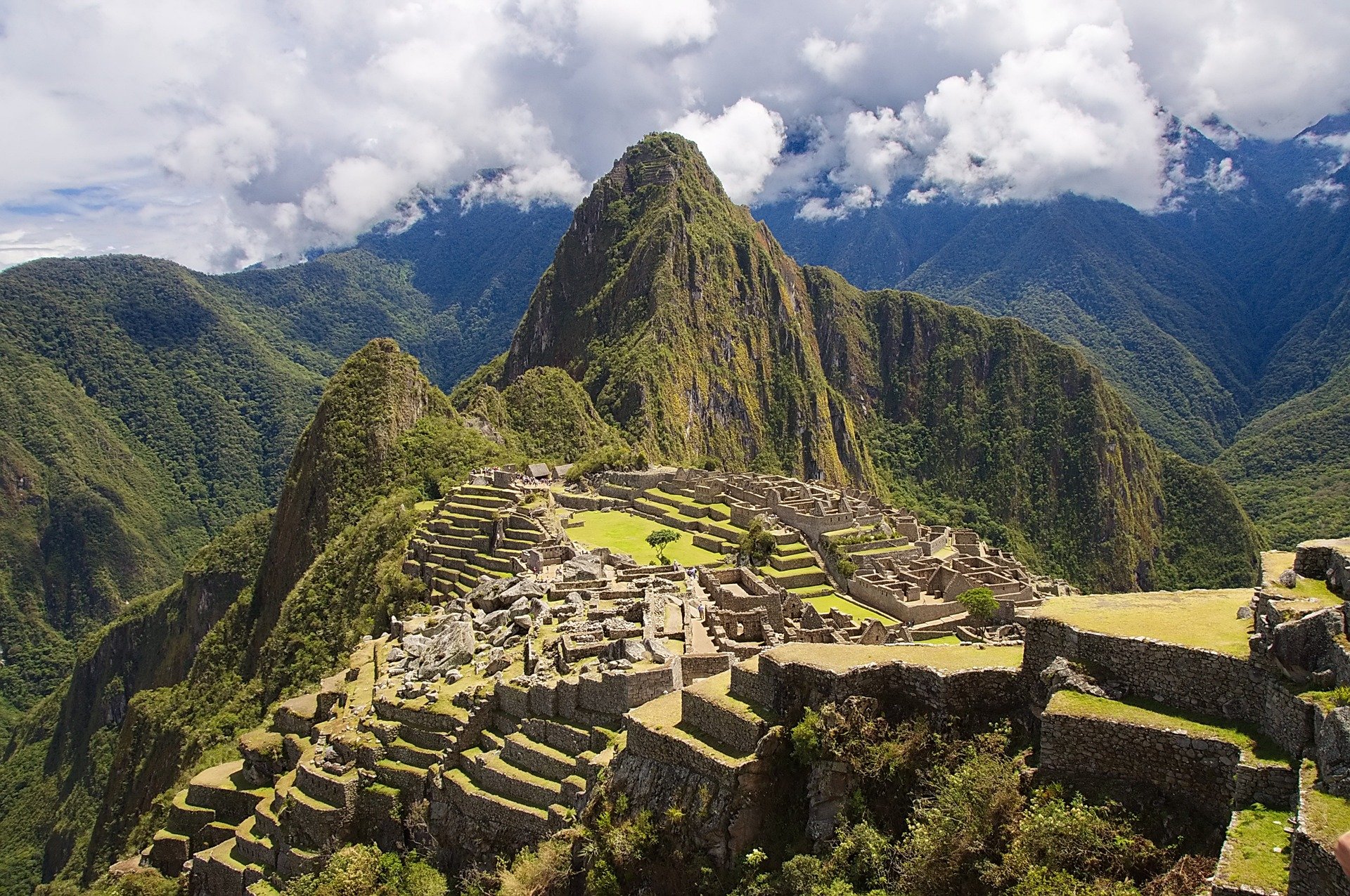 Ancient Inca ruins at Machu Picchu with lush green mountains and cloudy sky in the background.