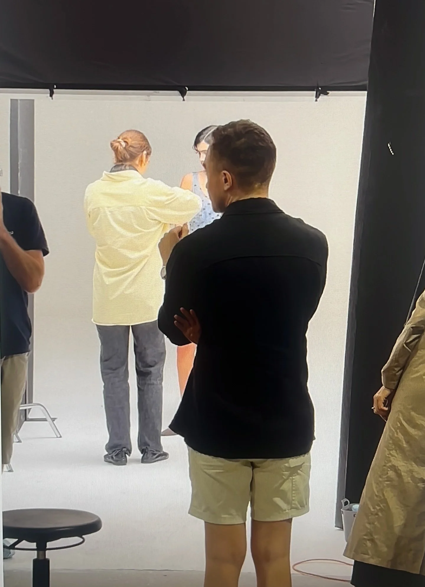 People gathered in a photography studio with a white background, some are adjusting a woman in a blue dress, while others stand and observe.
