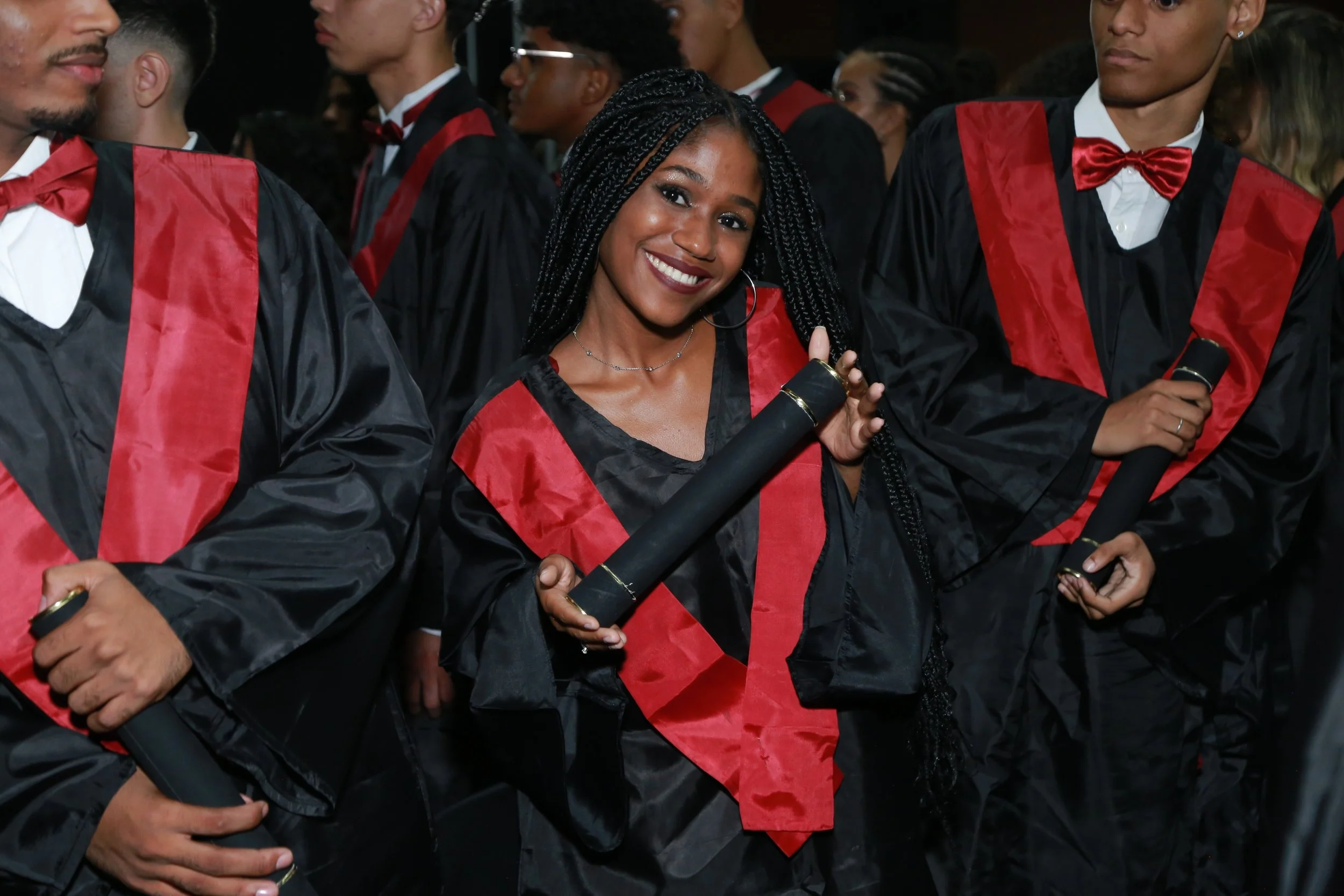 Grupo de estudantes de graduação em traje de formatura, usando beca, segurando diplomas, em uma cerimônia de formatura