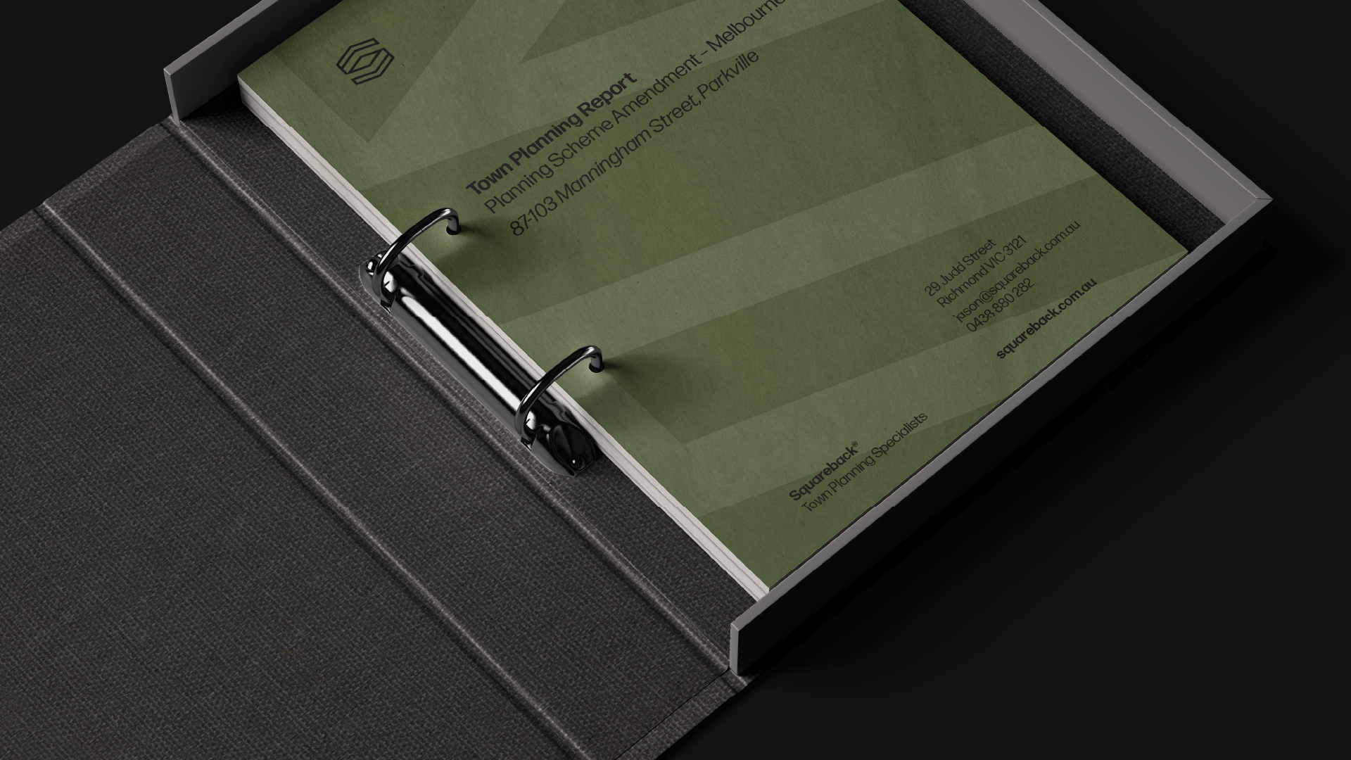 Open binder containing A3-sized green town planning report with black text, metal rings, and a black textured cover, placed on a black surface.