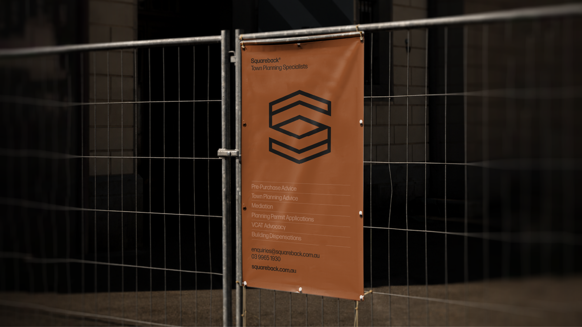 Orange banner attached to a metal fence displays information about Squareback Town Planning Specialists, listing services such as pre-purchase advice, town planning advice, mediation, planning permit applications, VCAT advocacy, and building dispensations, along with contact email, phone number, and website.