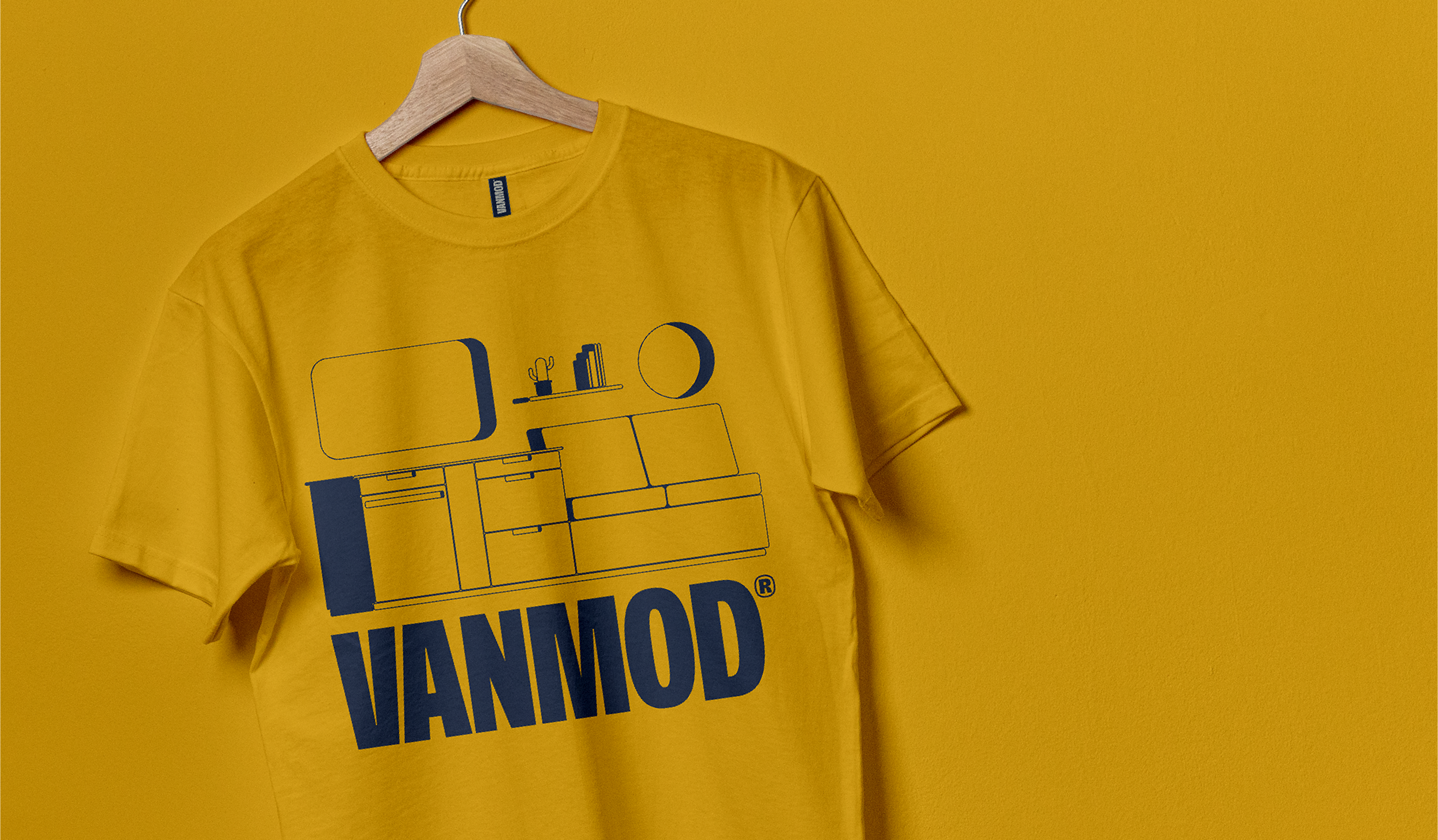 Yellow t-shirt hanging on a wooden hanger against a yellow wall with a graphic of a kitchen and the word 'HAMMOD' in bold blue letters.