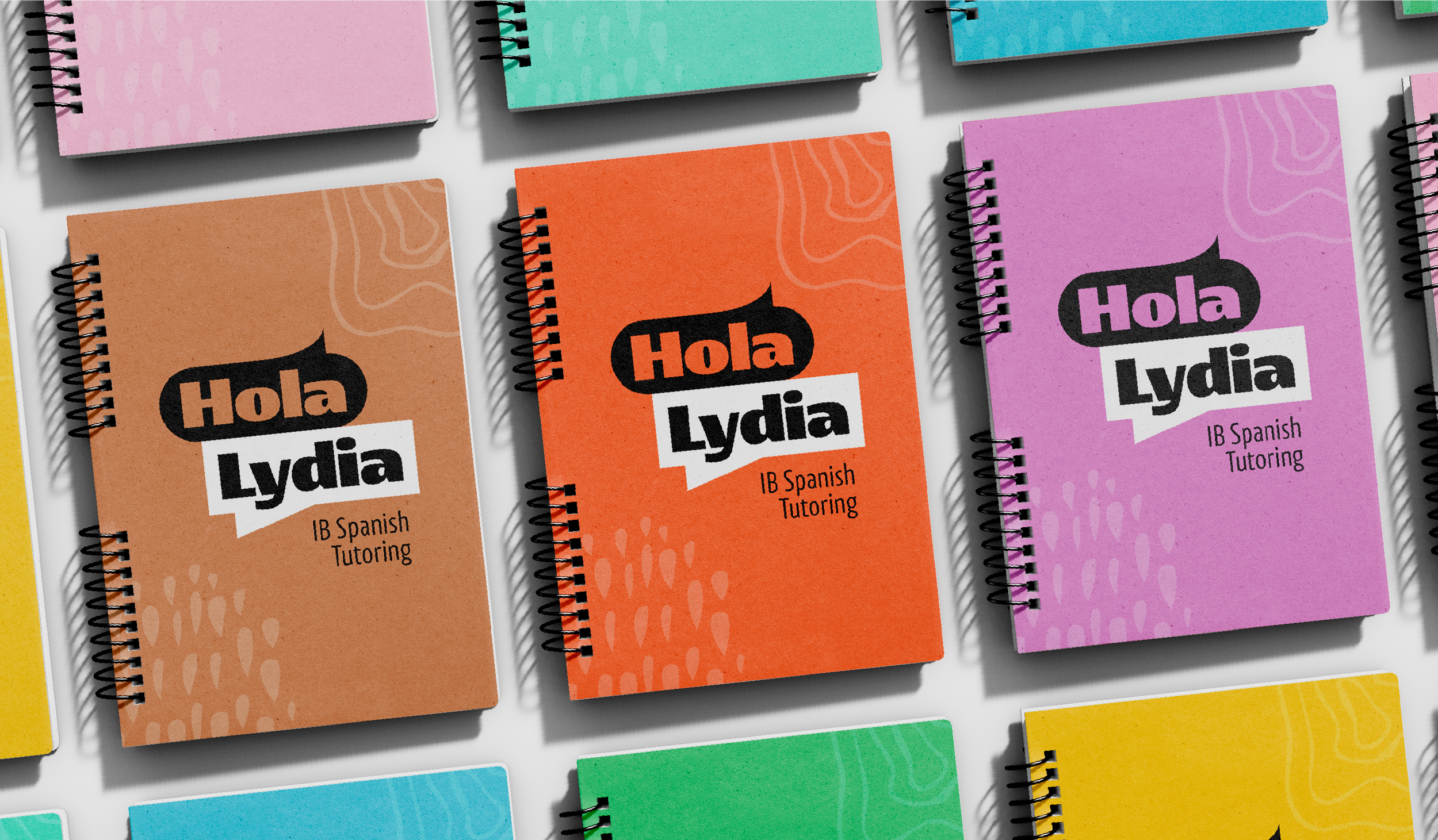 Colorful spiral-bound notebooks arranged on a white surface with the text "Hola Lydia" and "IB Spanish Tutoring" on their covers, featuring various colors such as peach, orange, and purple.
