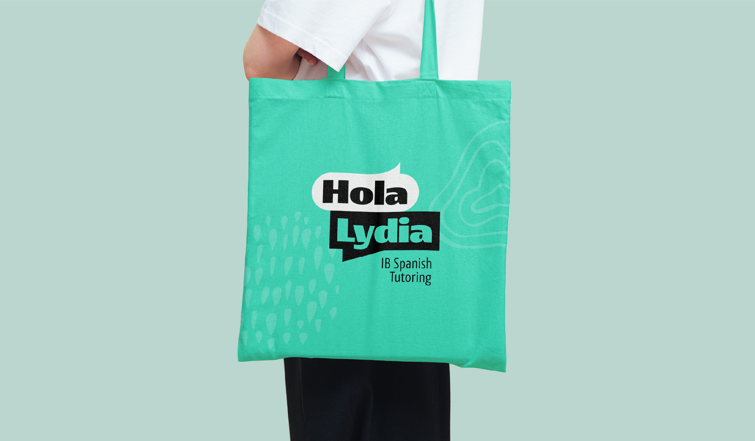 A person holding a turquoise tote bag with black and white text that reads 'Hola Lydia IB Spanish Tutoring,' against a matching light turquoise background.