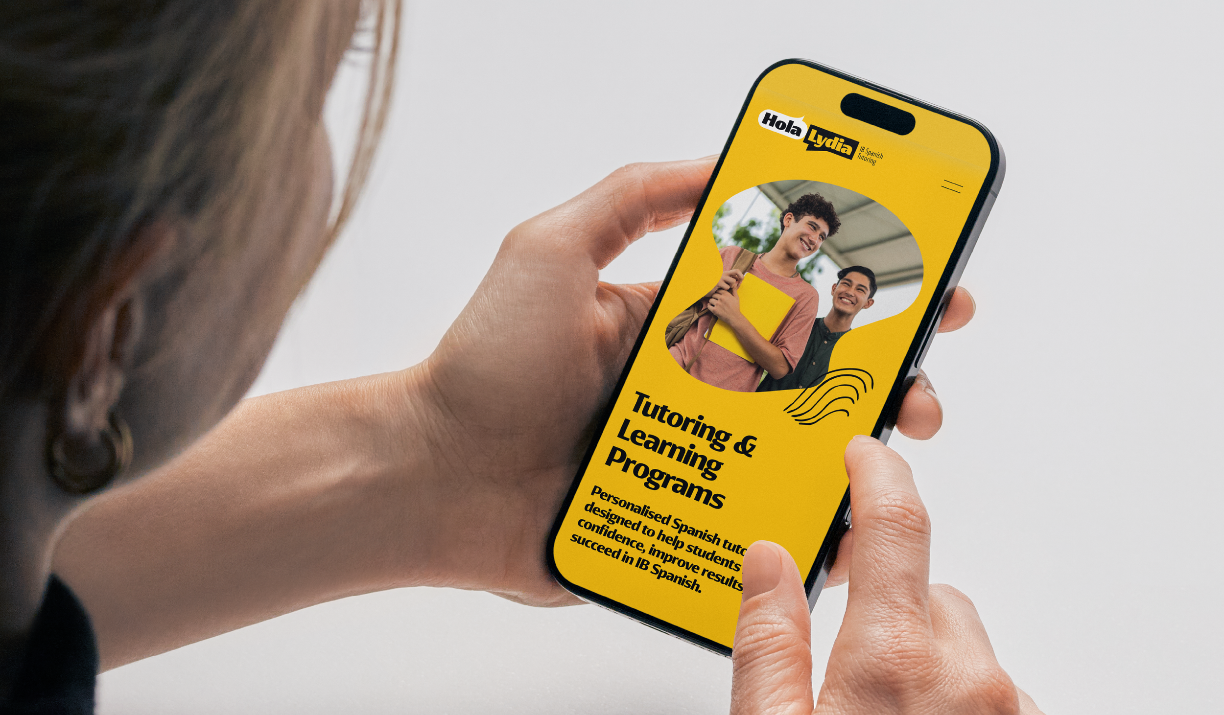 Person holding a smartphone with an app for tutoring and learning programs, showing two smiling students on the screen with a yellow background.