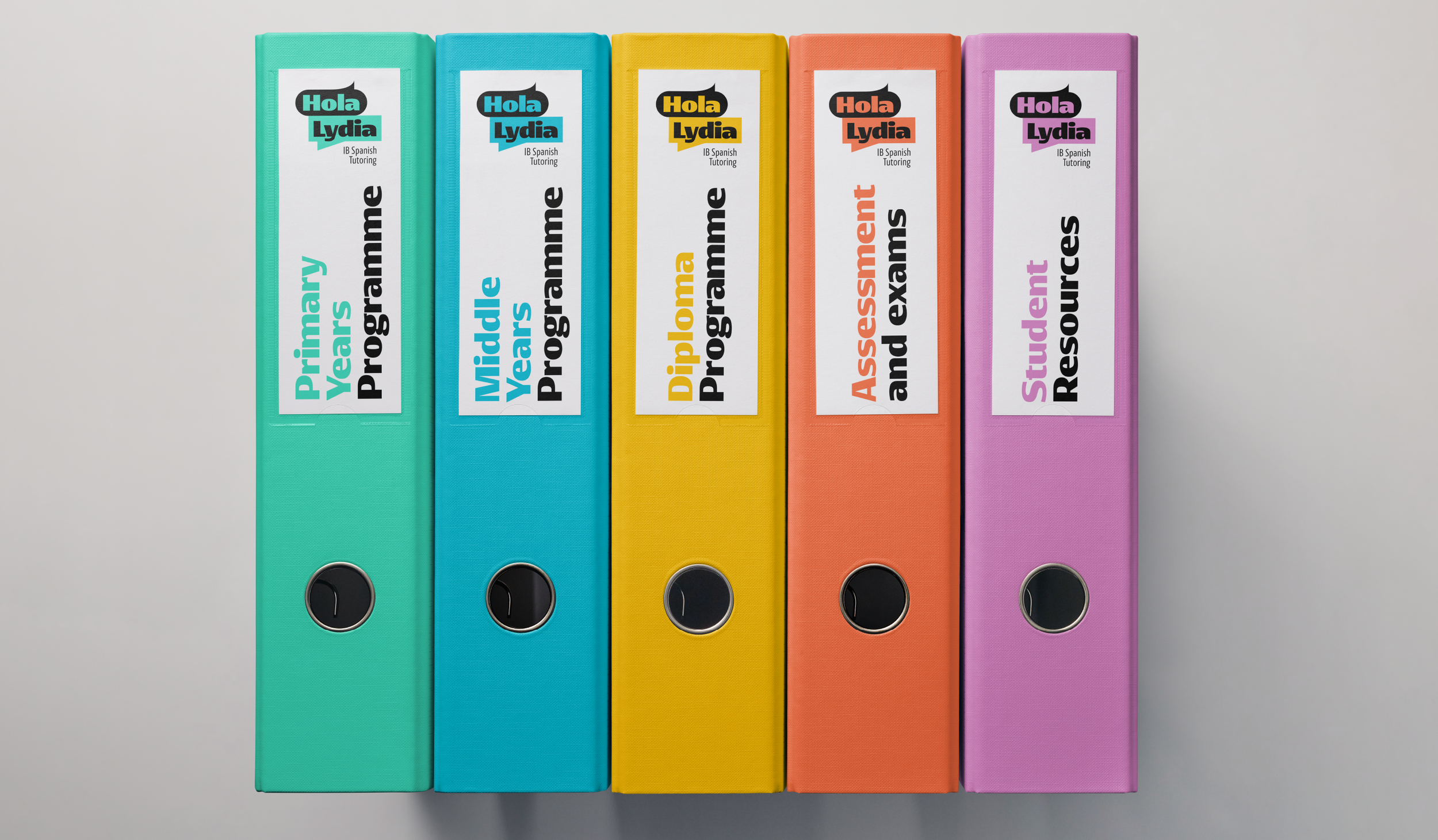 Five colorful binders standing vertically in a row on a gray surface. Each binder has a white label with text, and the titles read from left to right: "Primary Years Programme," "Middle Years Programme," "Diploma Programme," "Assessment and extern" (partially cut off), and "Student Resources."