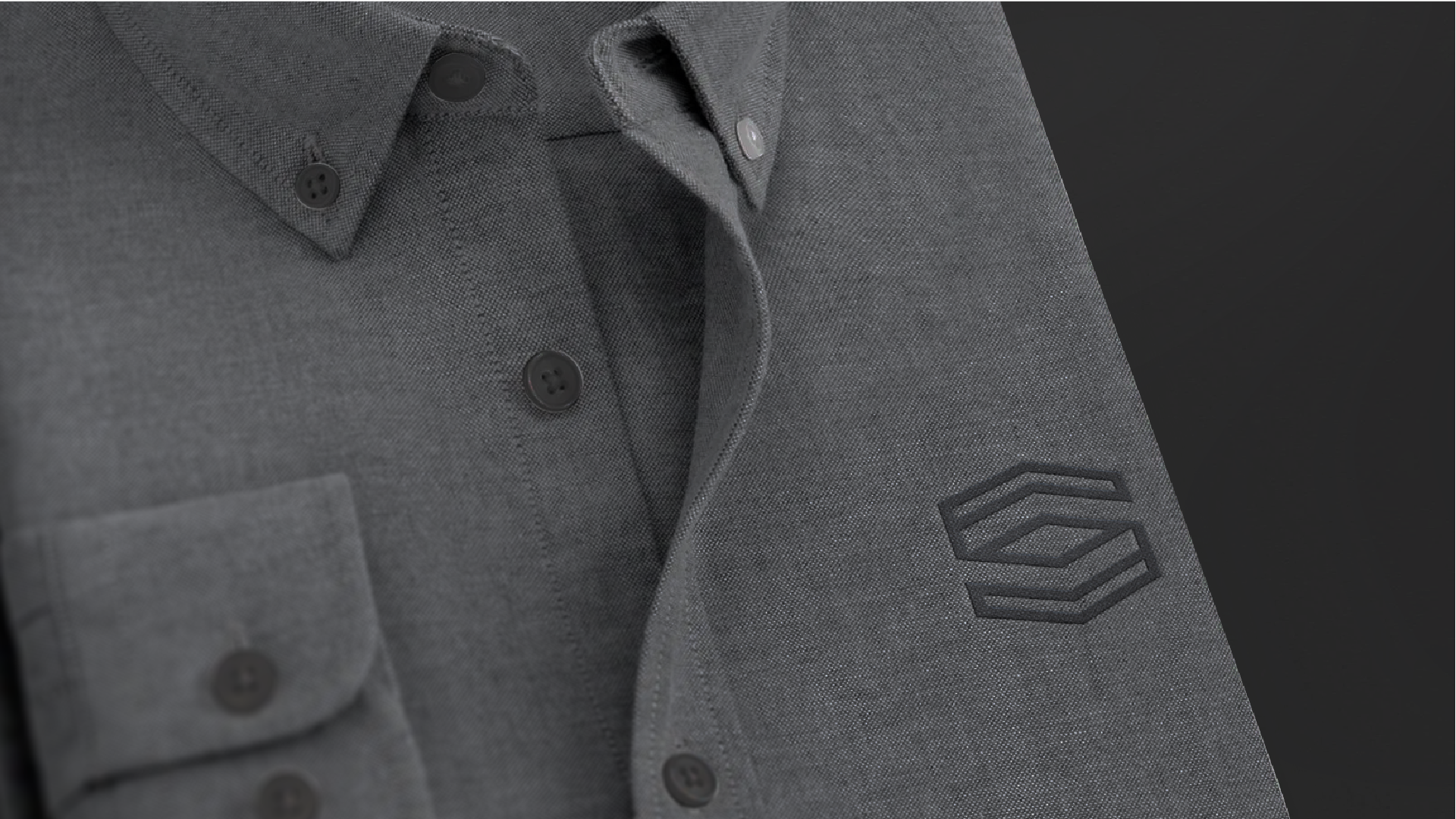 Close-up of a gray polo shirt featuring black buttons, a collar, and an embroidered hexagonal logo on the sleeve.