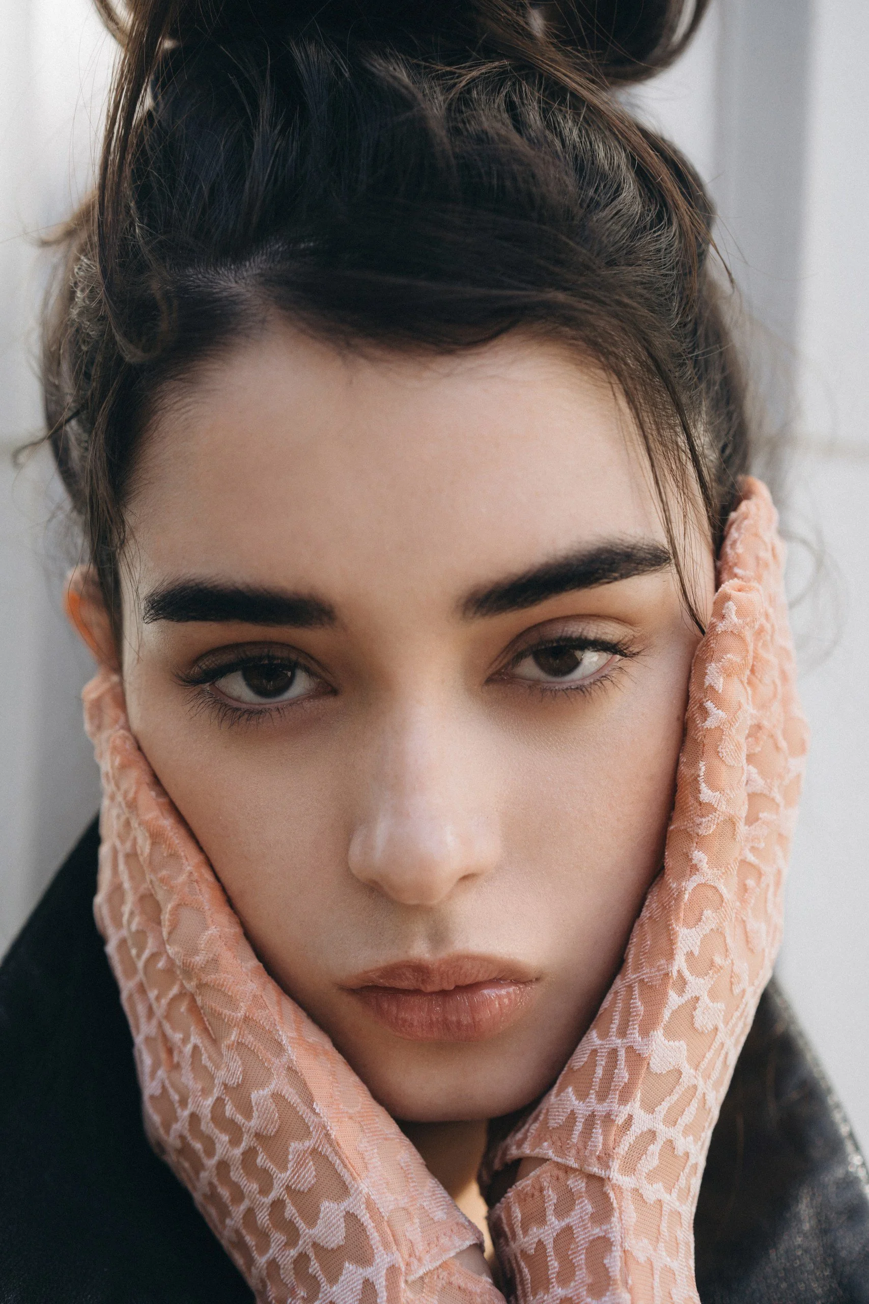 Close-up of a person's face, with dark hair and eyebrows, resting on a peach-colored lace scarf around their neck, with a neutral expression.