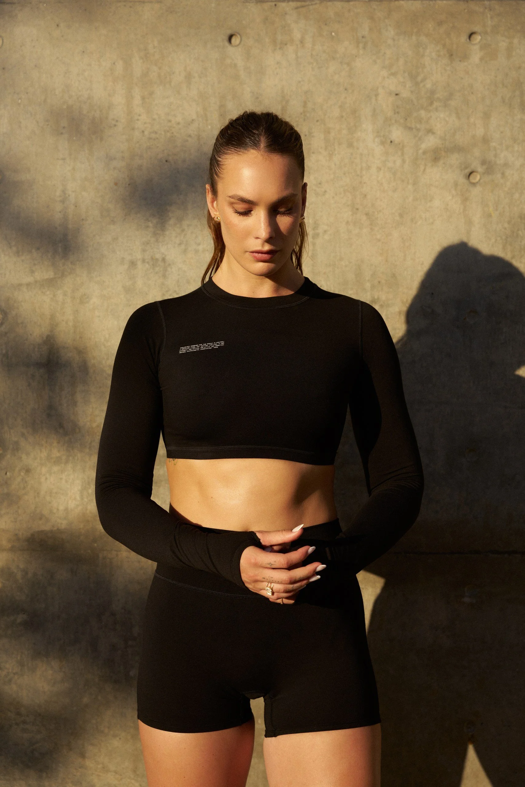 Young woman in black workout attire standing in front of a concrete wall with shadows cast on it