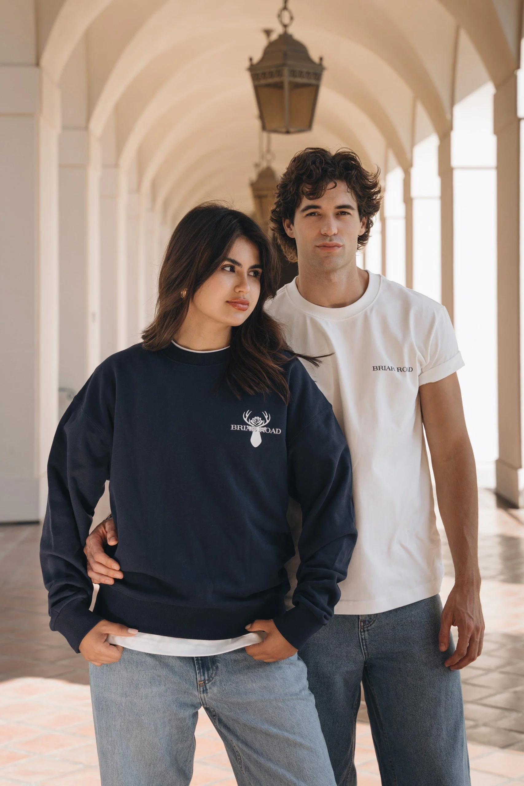 A man and woman walking through an arched corridor, both wearing casual clothing with the word 'Briar Road' on their shirts.