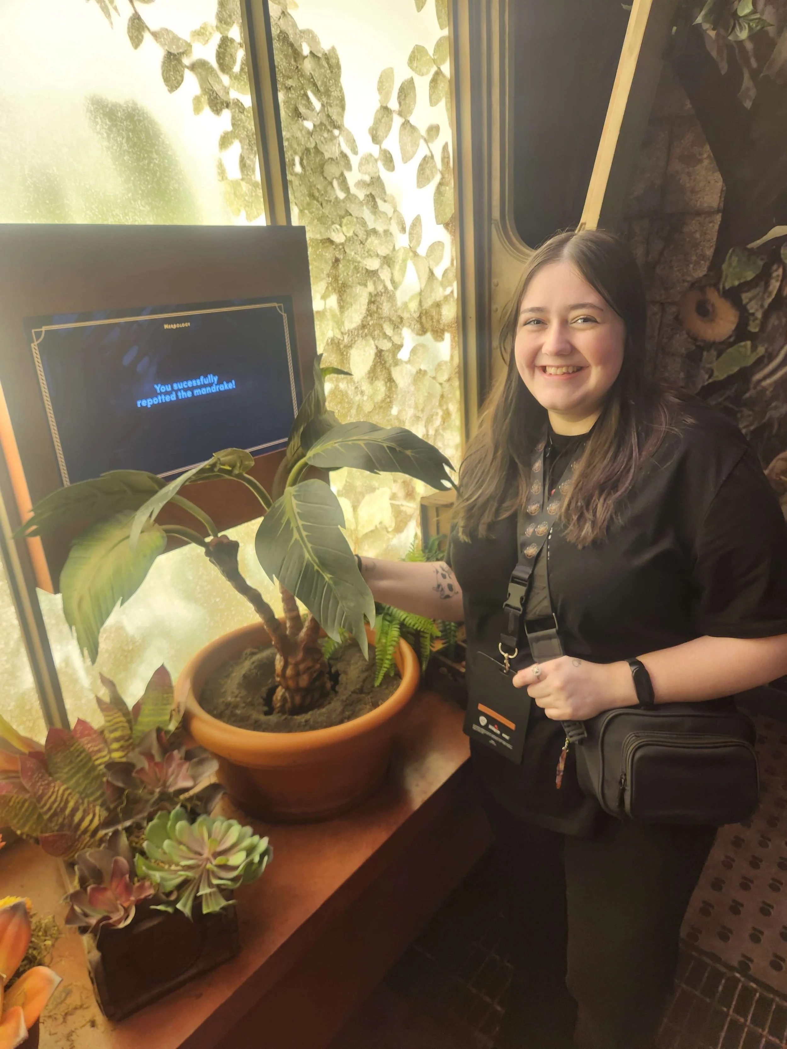 Salem smiling at a potted mandrake in an indoor setting, with a monitor showing a message about a successful mandrake report.
