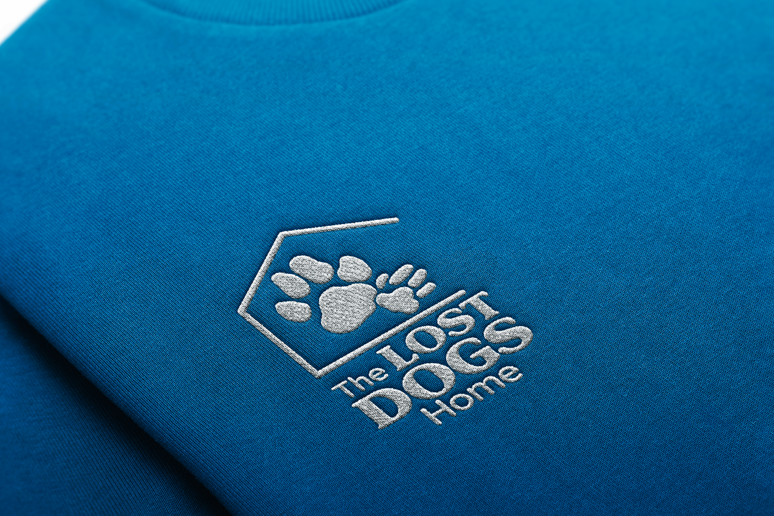 A close-up of a blue fabric with an embroidered logo showing a paw print and the text 'The Lost Dogs Home'.