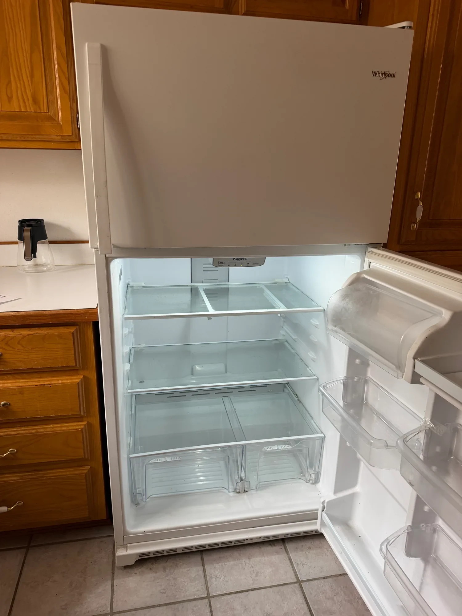  Open white refrigerator next to oak kitchen cabinets 