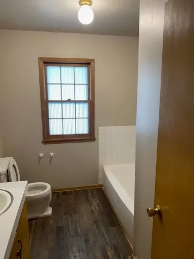  Bathroom with bathtub, toilet, vanity, and a frosted window 