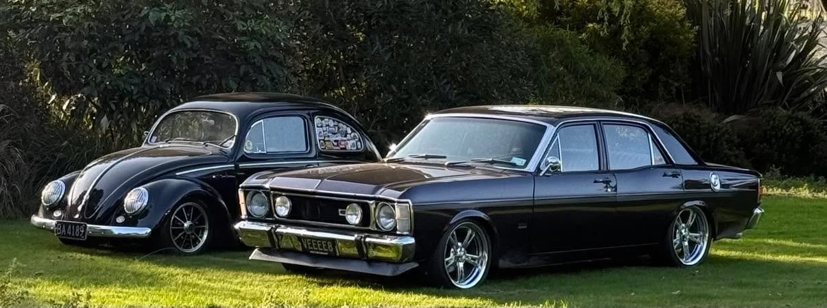 Two vintage black cars parked on a grassy area with trees in the background.