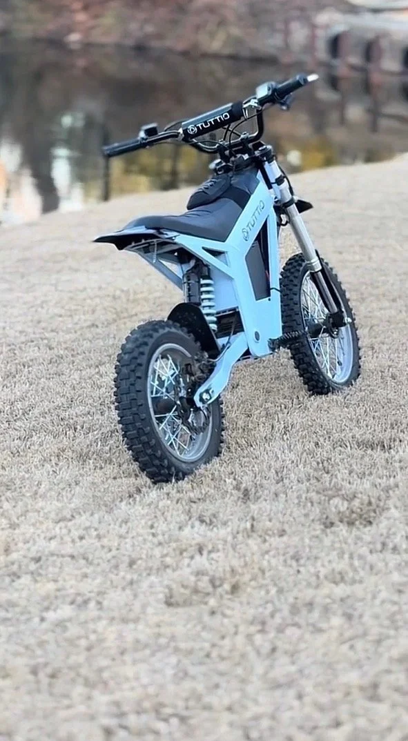 Electric dirt bike with thick knobby tires on beige grass near a body of water.