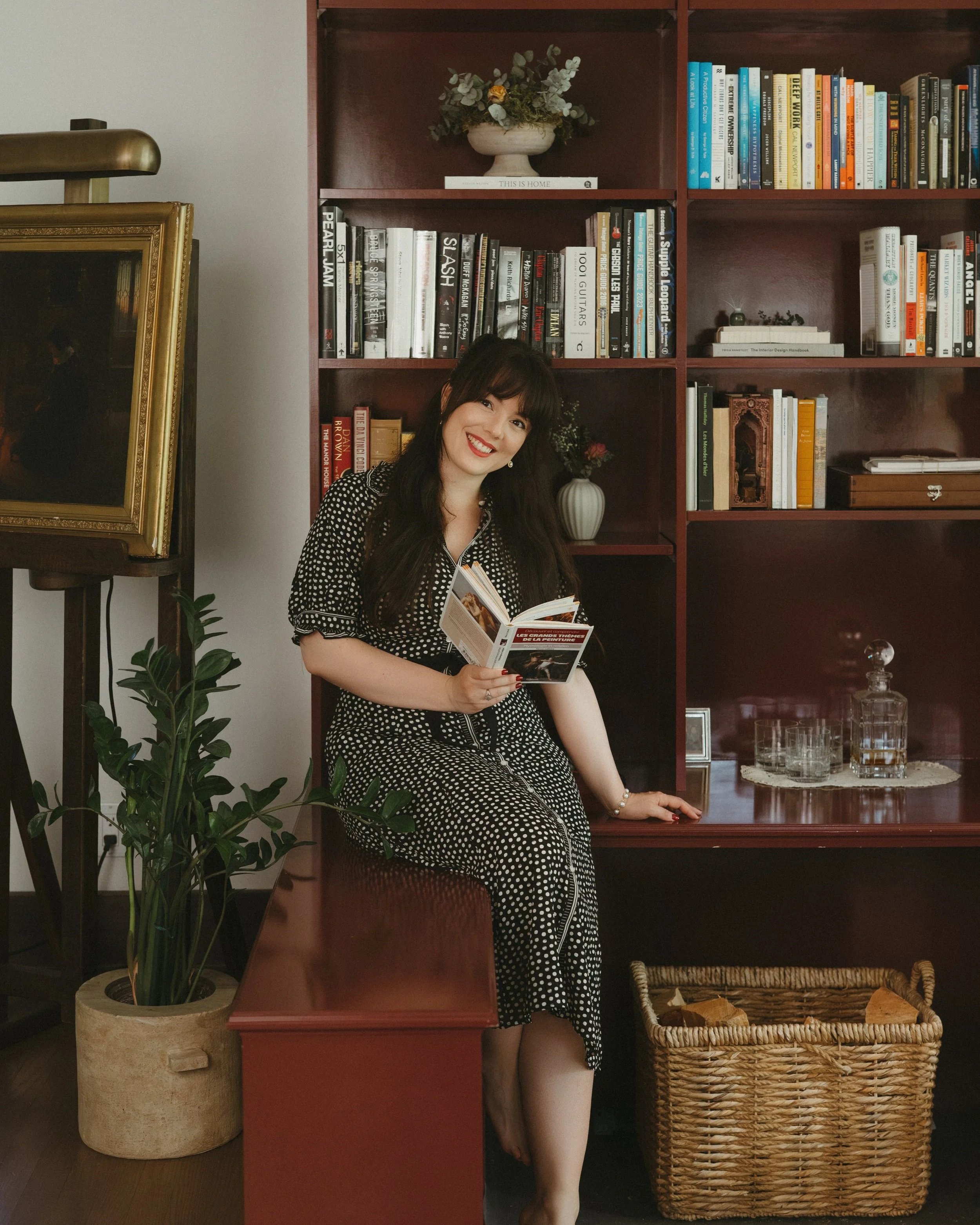 Photo of Iris Humbert standing next to a dark wooden bookshelf filled with books and thoughtfully layered decor.