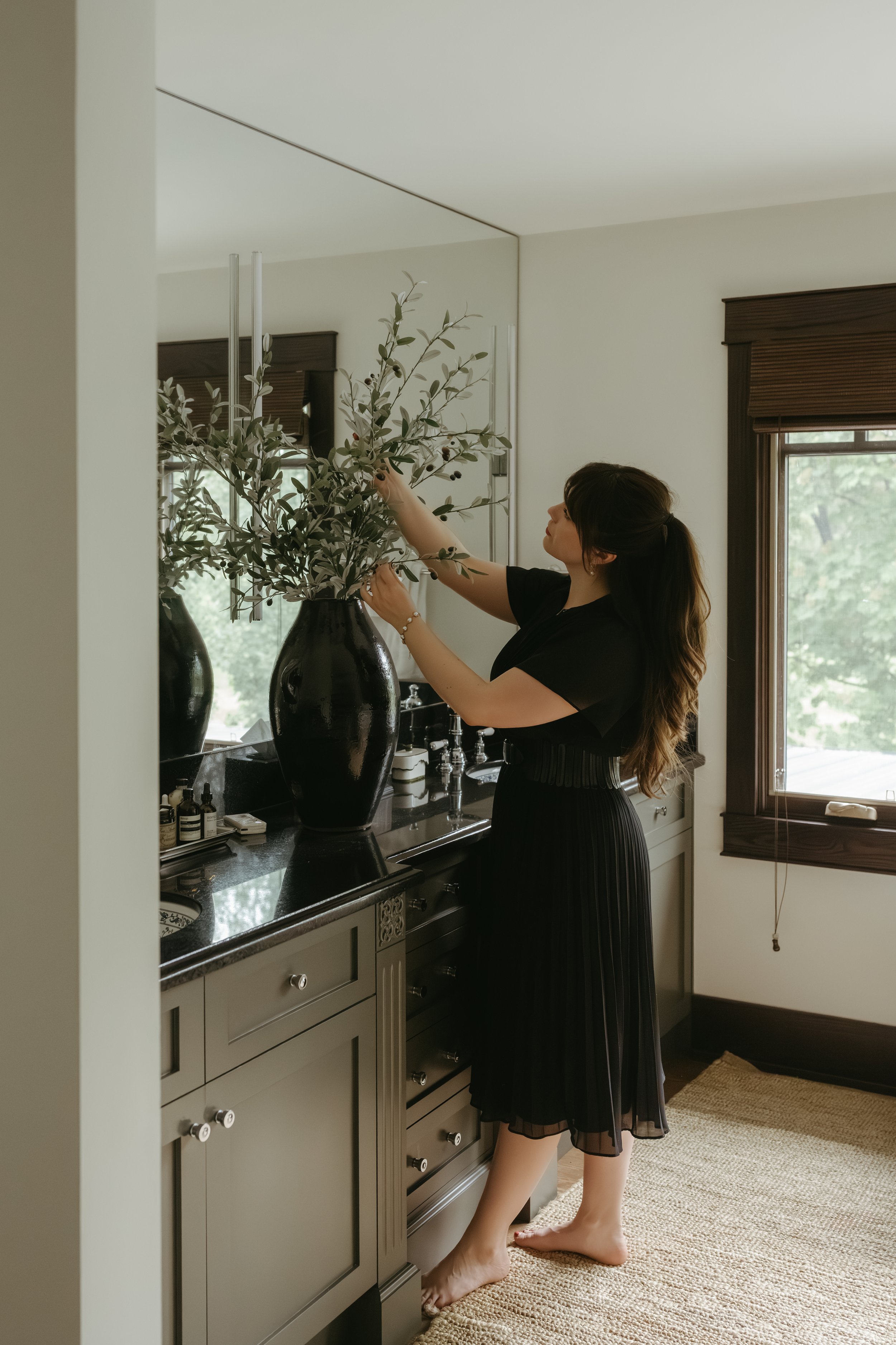 Iris Humbert carefully styling a tall vase of branches and greenery to create the perfect finishing touch. Every detail is thoughtfully considered and intentionally placed, reflecting a refined commitment to quality, 