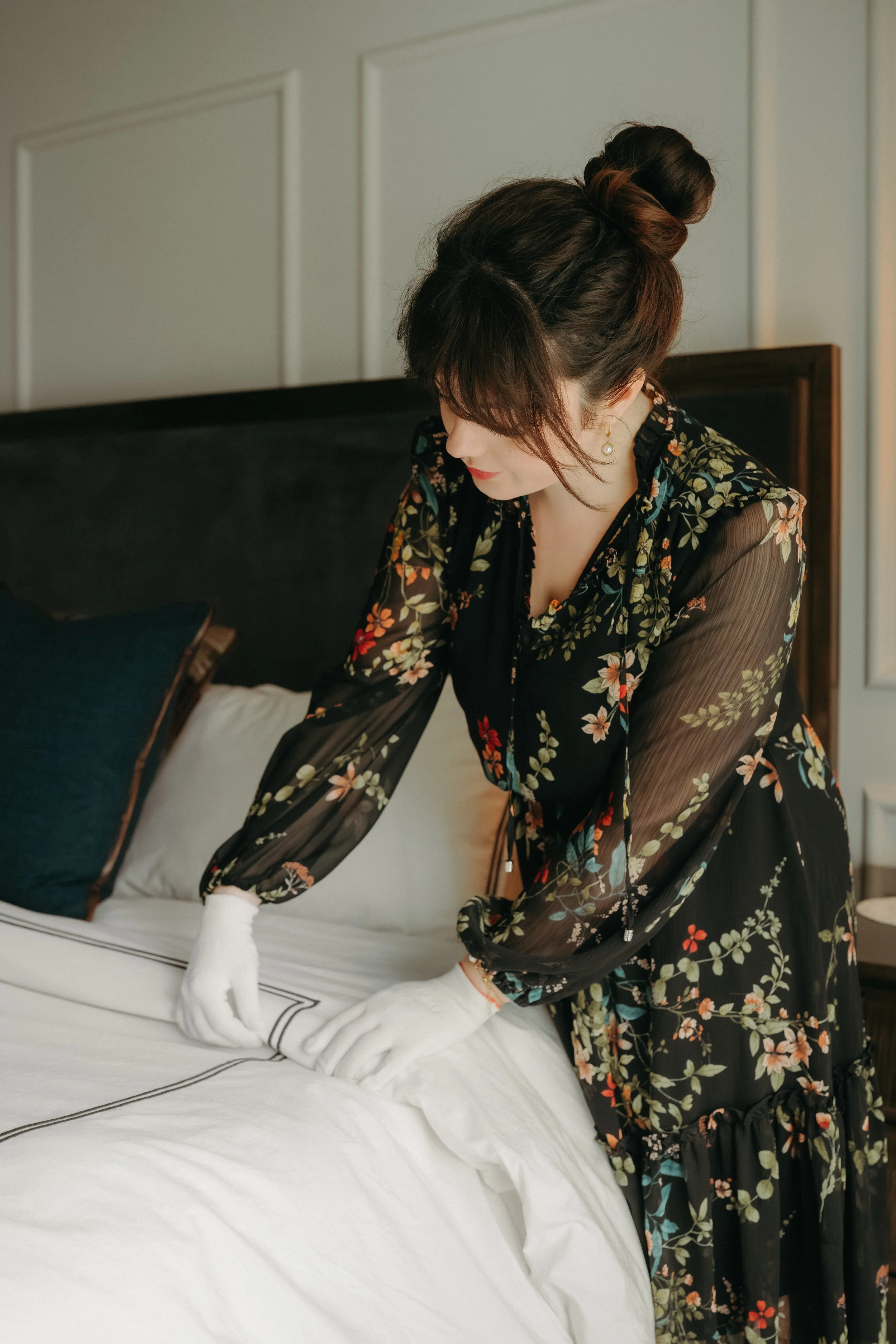 Iris Humbert wearing white gloves and thoughtfully styling the layers of a bed, paying attention to every detail.