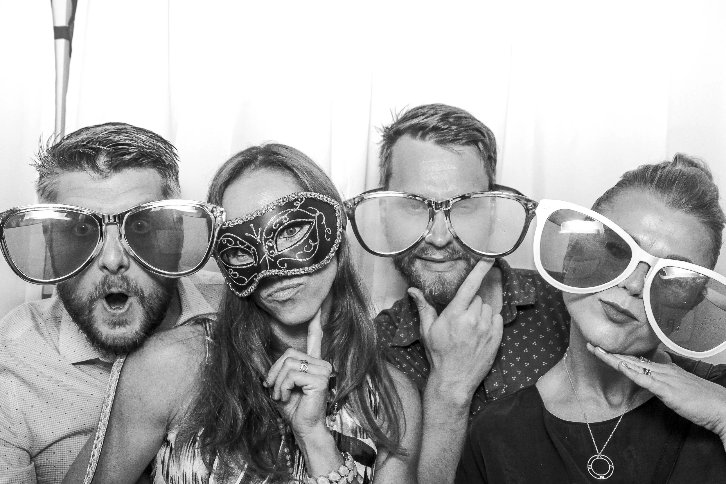 Group of five people wearing large novelty glasses and masks, posing for a photo in a photo booth.
