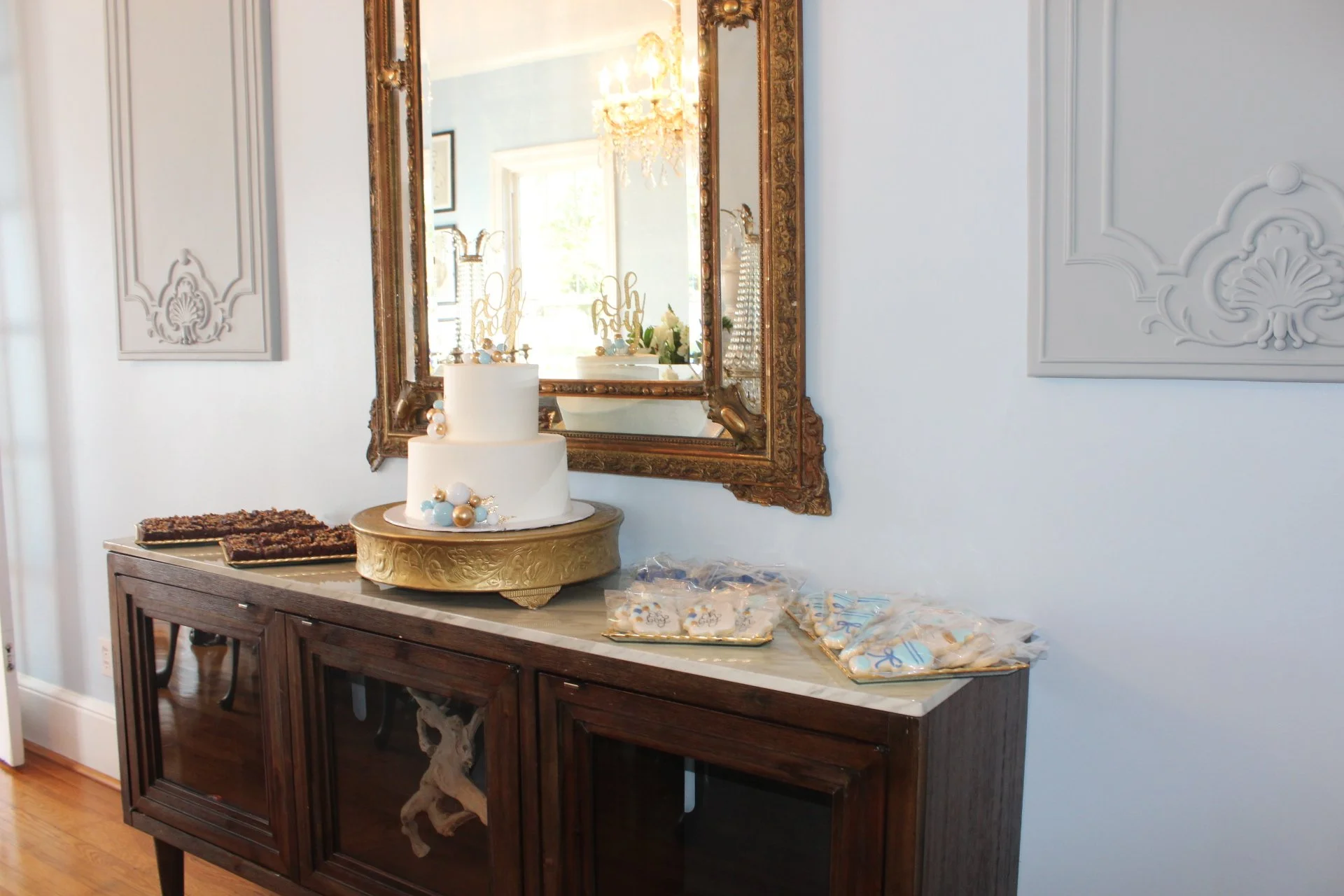 Baby shower dessert table with tiered cake and cookies under a gilded mirror at Amelie Beau