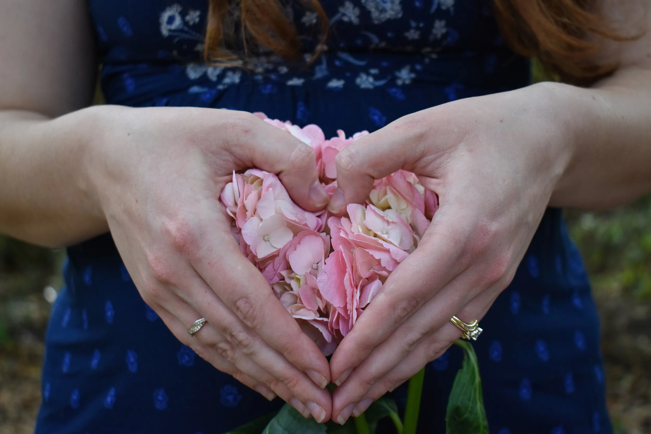 Person making a heart shape with hands filled with pink and cream flower petals.
