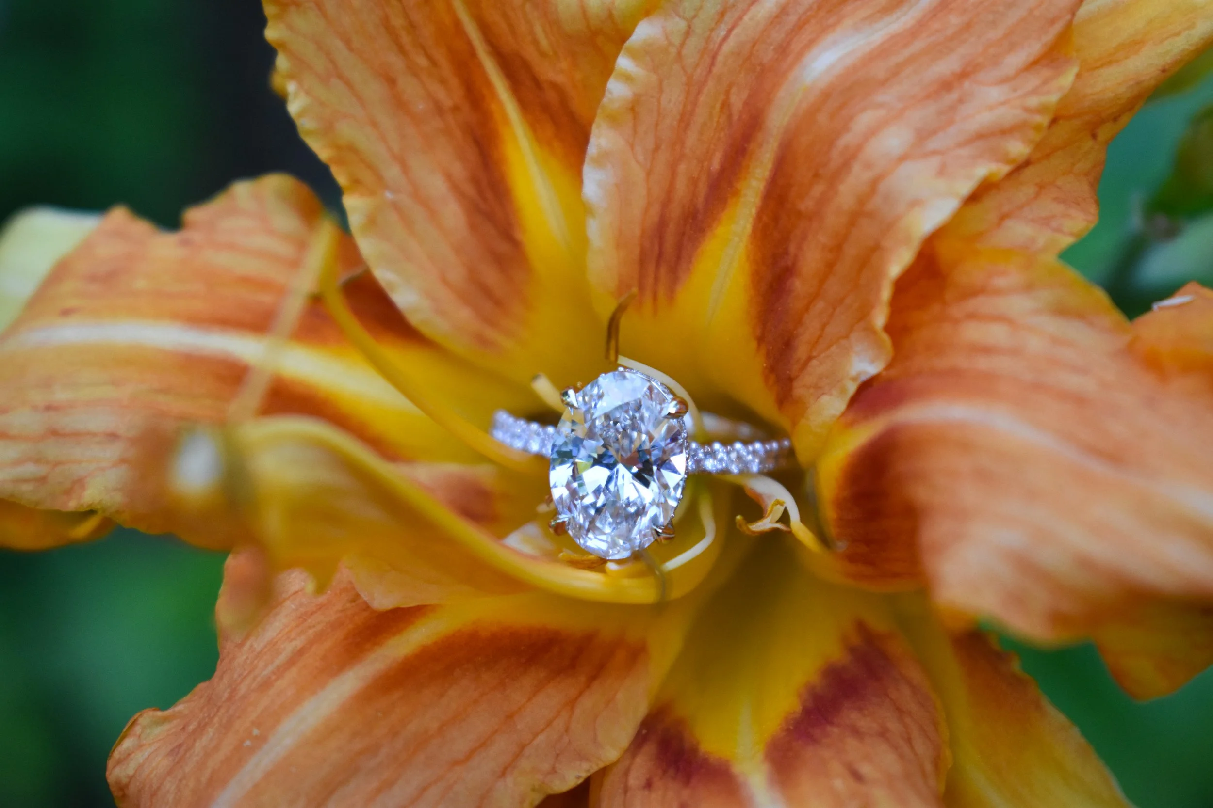 A close-up of a diamond ring with a large central gemstone, set inside a vibrant orange and yellow flower.