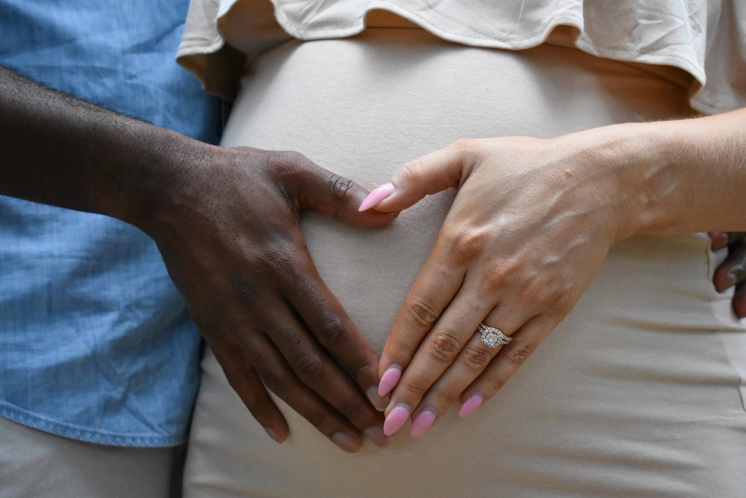 Close-up of two hands, one dark-skinned and the other light-skinned, gently placed on a pregnant belly, showing support and care.