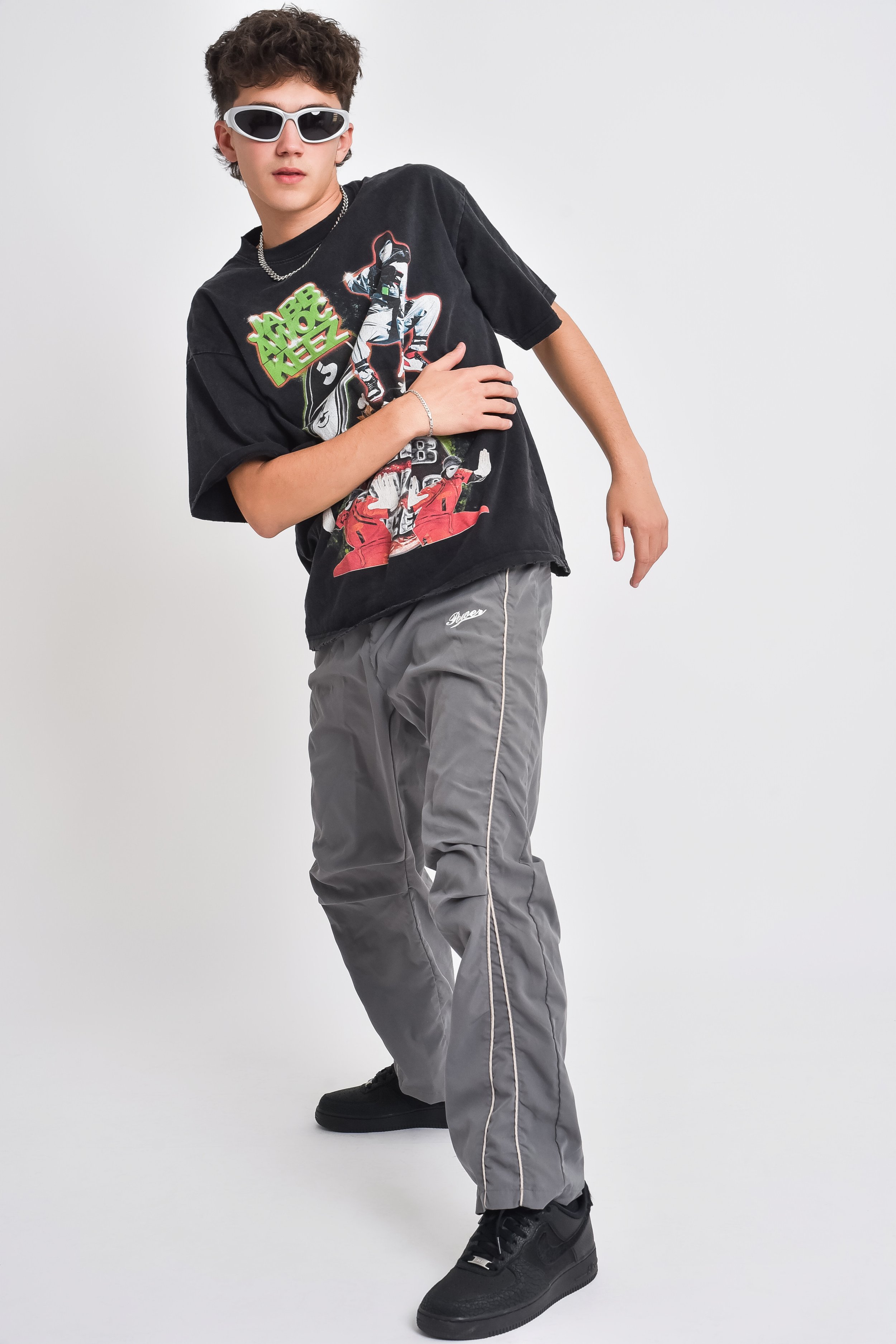 A young person wearing black Nike sneakers, gray baggy pants, a graphic black T-shirt featuring a character from Star Wars, and white sunglasses against a plain white background.