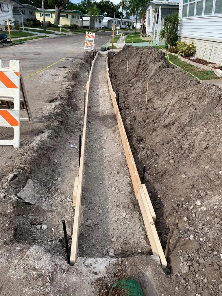 Construction site with trenches and wooden forms for curb or sidewalk installation in a residential neighborhood.
